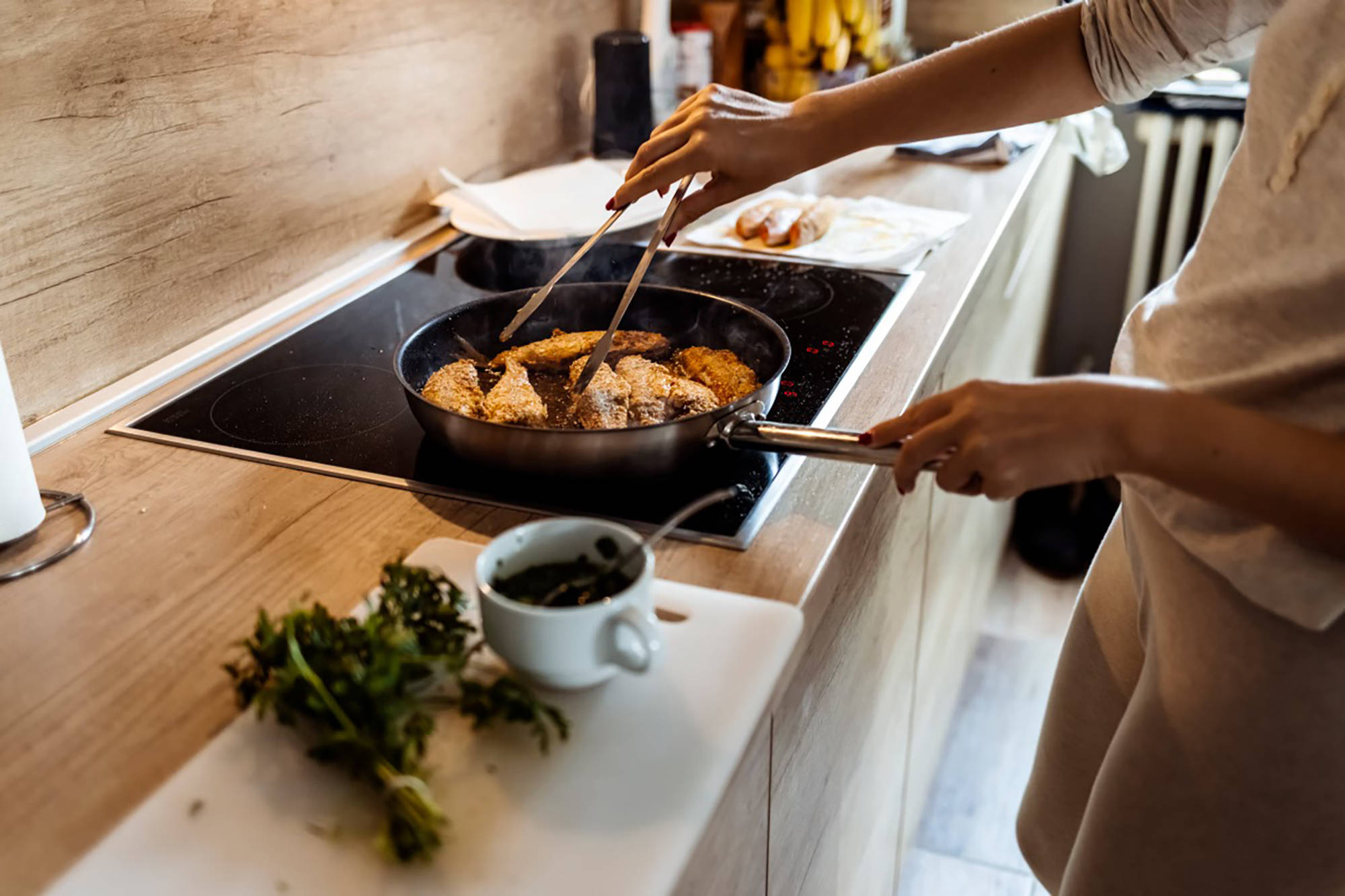 Eine Person brät in einer Pfanne Fisch an und wendet die Filets mit einer Zange. 