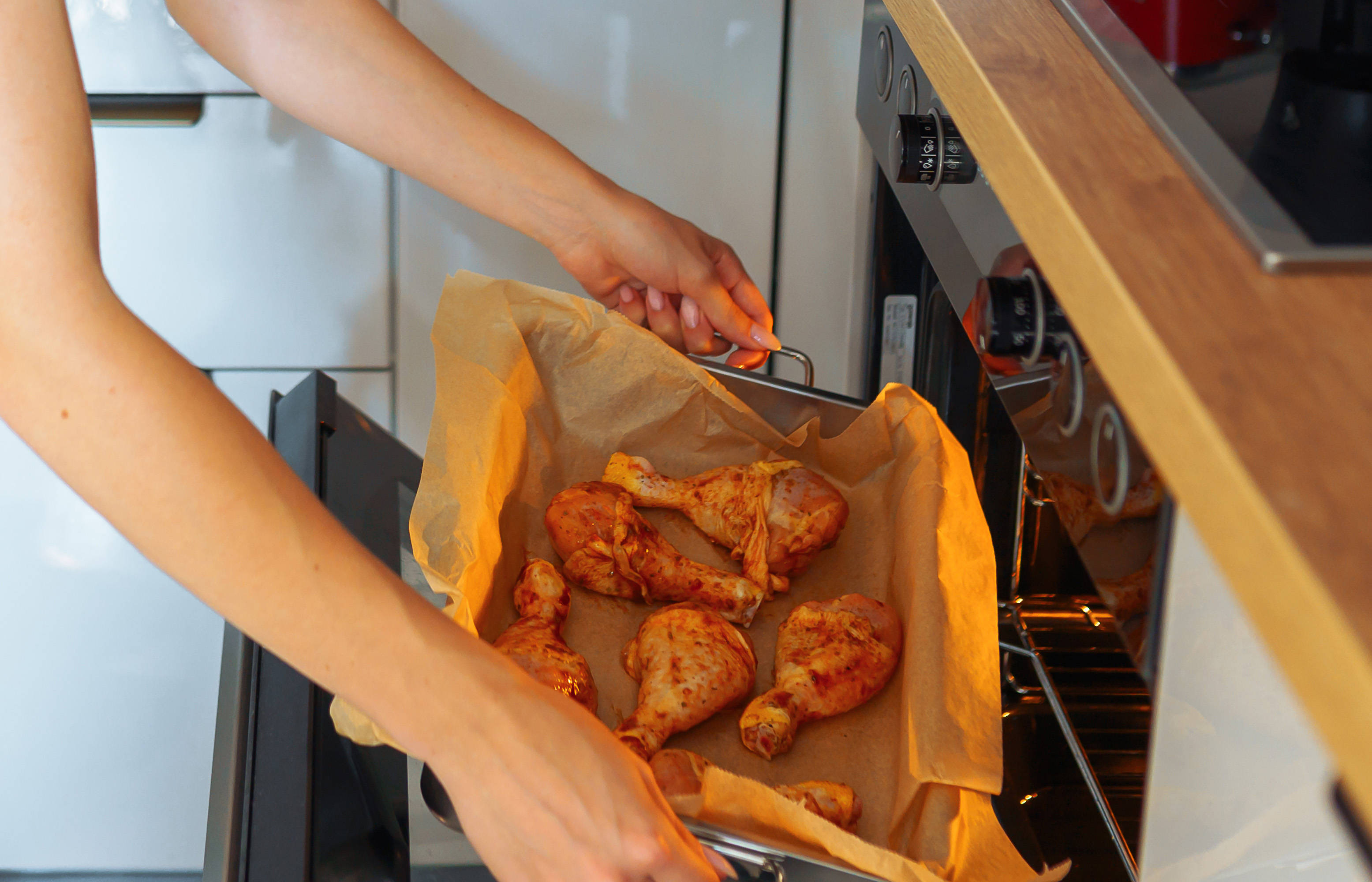 Eine Frau schiebt ein Blech mit marinierten Hähnchen Käulen in den Backofen.