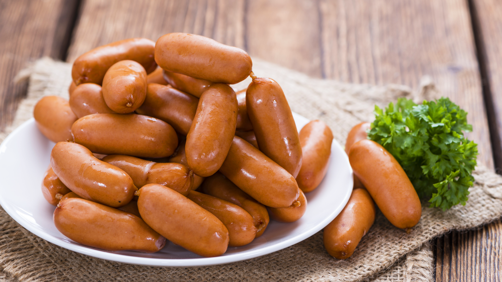 Teller mit Würstchen und Petersilie auf Jute Stoff.