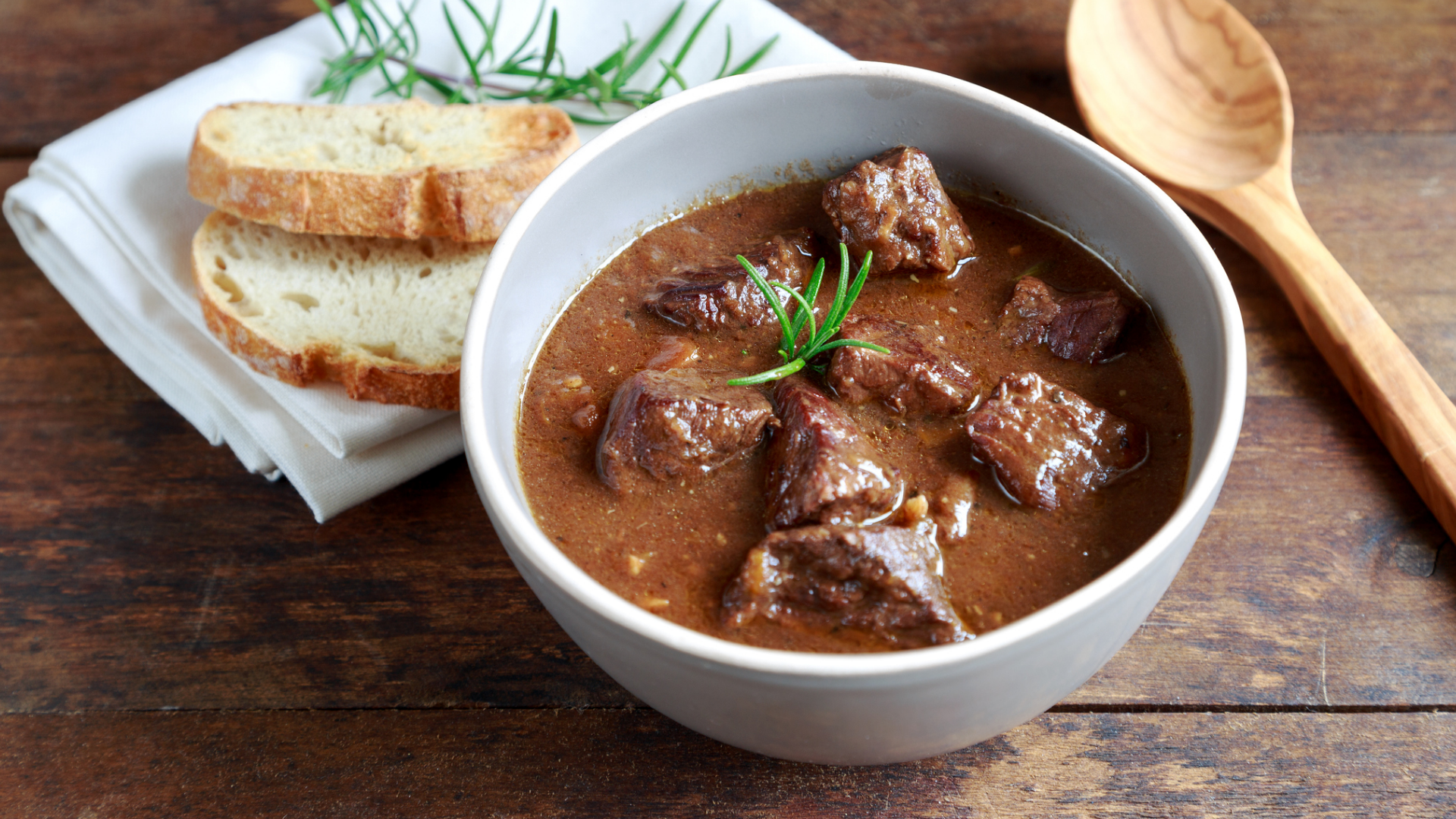 Fleischragout mit Brot und Holzlöffel auf rustikalem Holztisch.