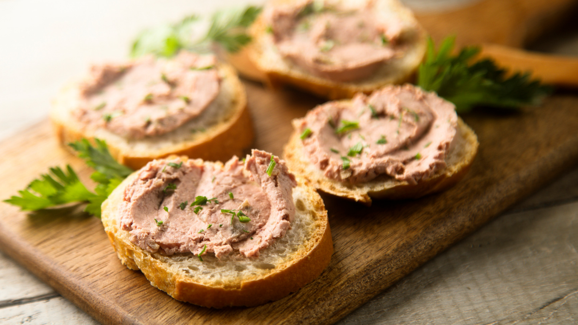 Brötchen mit Leberwurst auf Holzbrett, mit Kräutern.