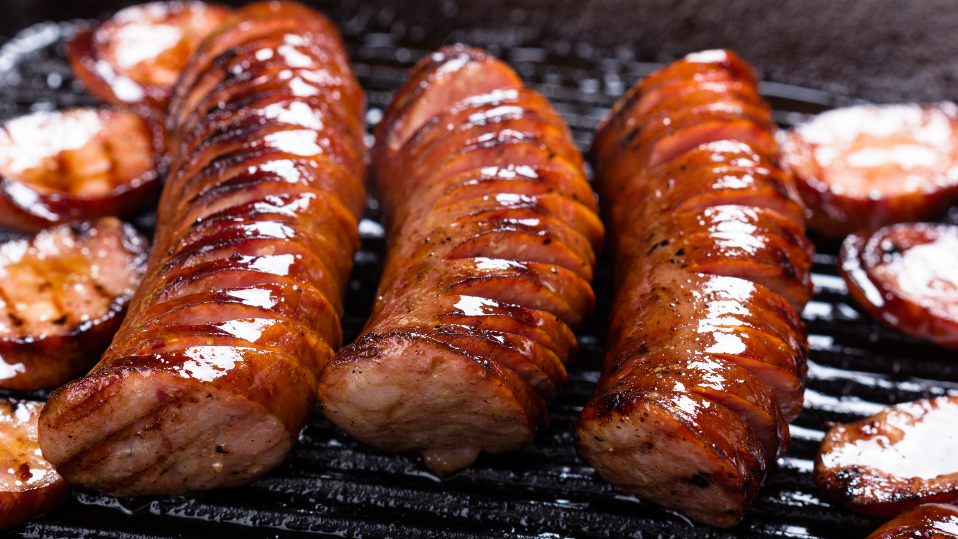 Drei gegrillte, eingeritzte Würste auf schwarzem Grillrost.