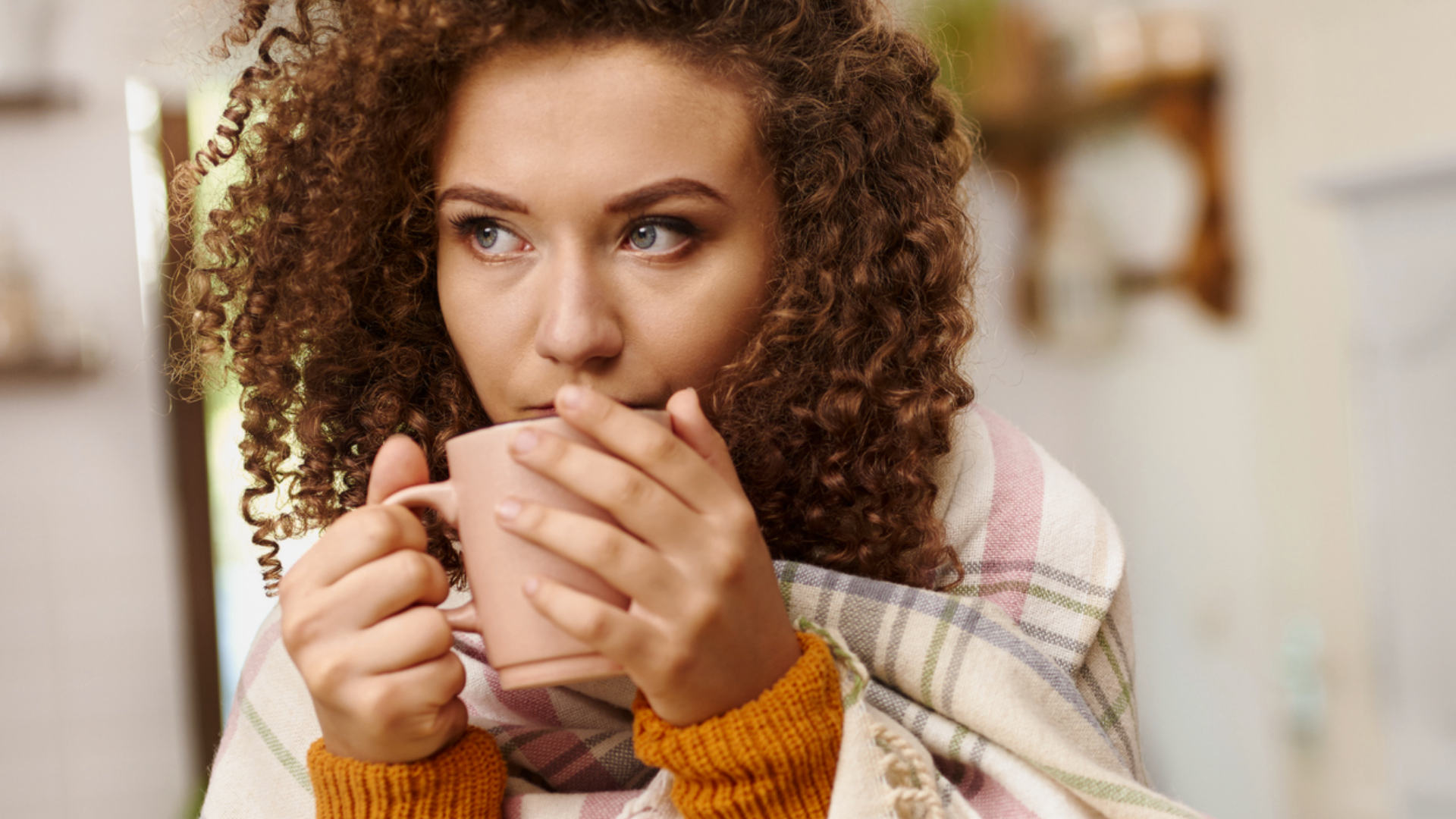 Frau mit Decke und Tasse in den Händen.