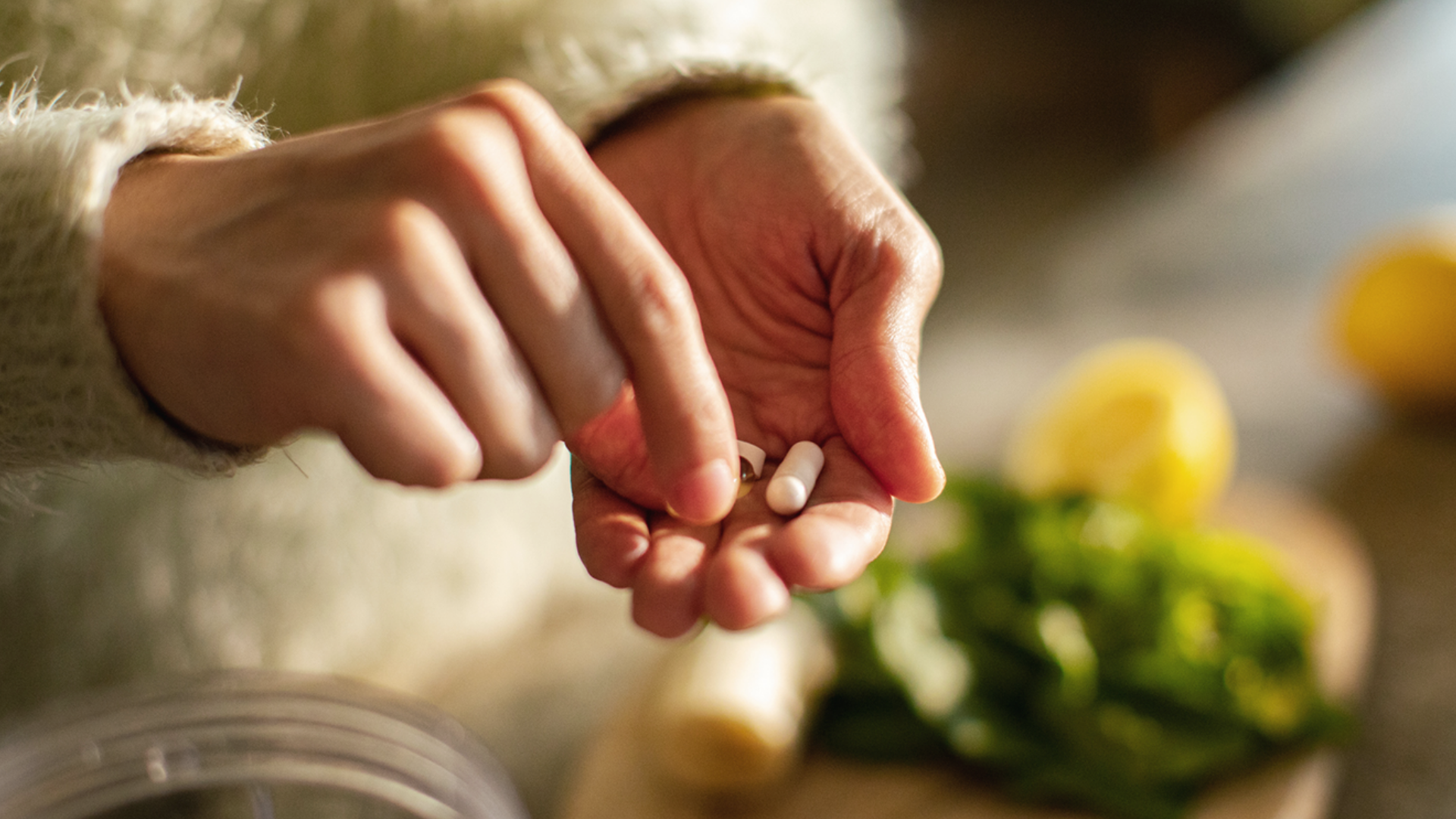 Hände halten Tabletten, Zitrone und Grünzeug im Hintergrund.
