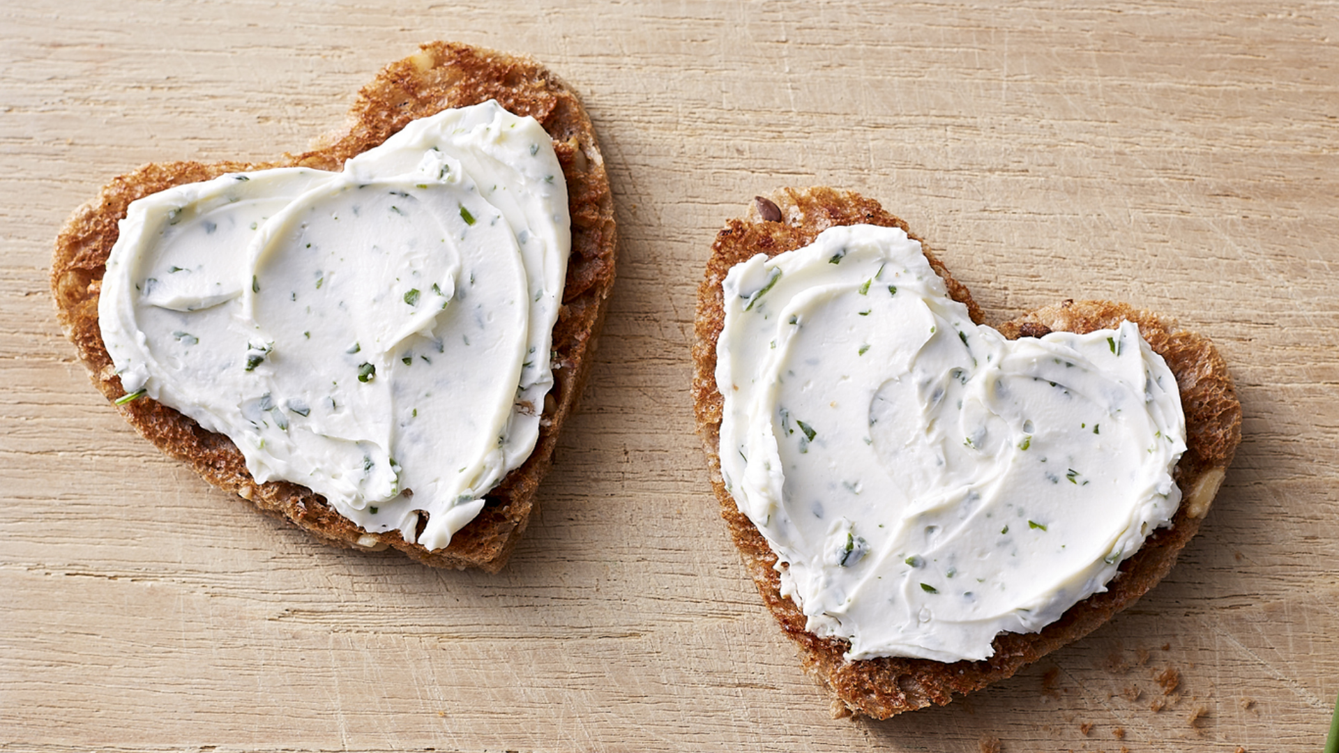 Herzförmiges Brot mit Kräuterfrischkäse auf Holzbrett.