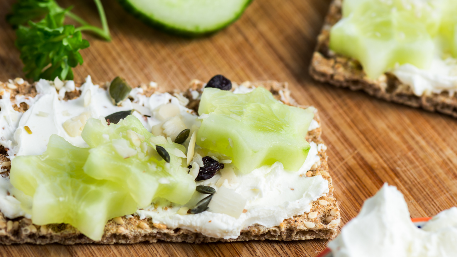 Knäckebrot mit Frischkäse, Gurke und Samen auf Holzbrett.