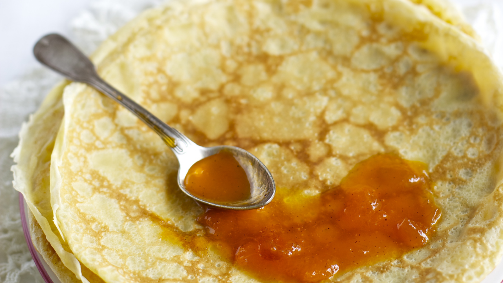 Crêpes mit Orangen-Fruchtaufstrich und Löffel.