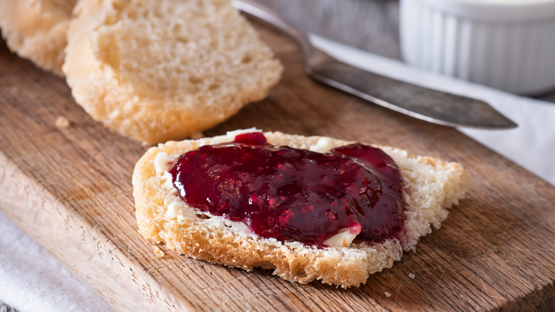 Brot mit rotem Fruchtaufstrich auf Holzbrett.