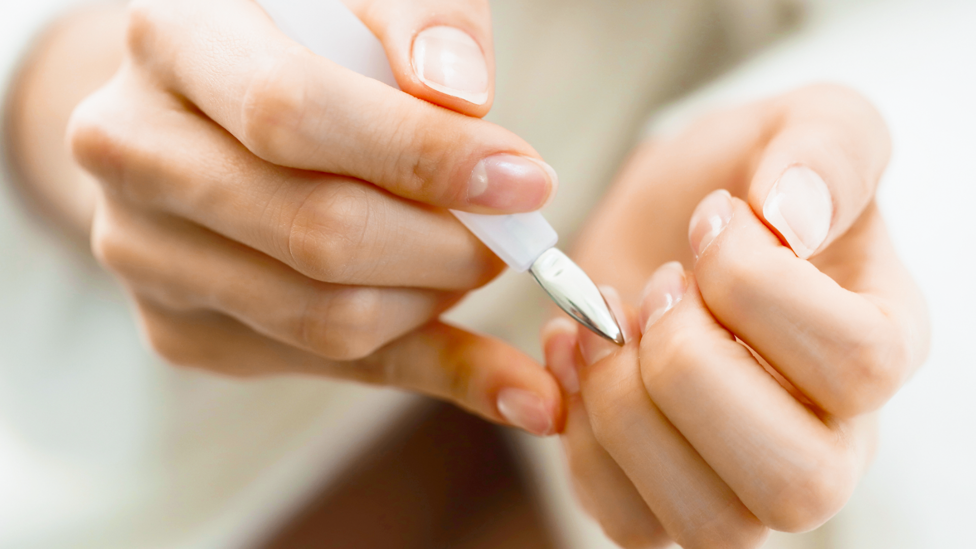 Hände benutzen einen Nagelhautschieber für Nagelpflege.