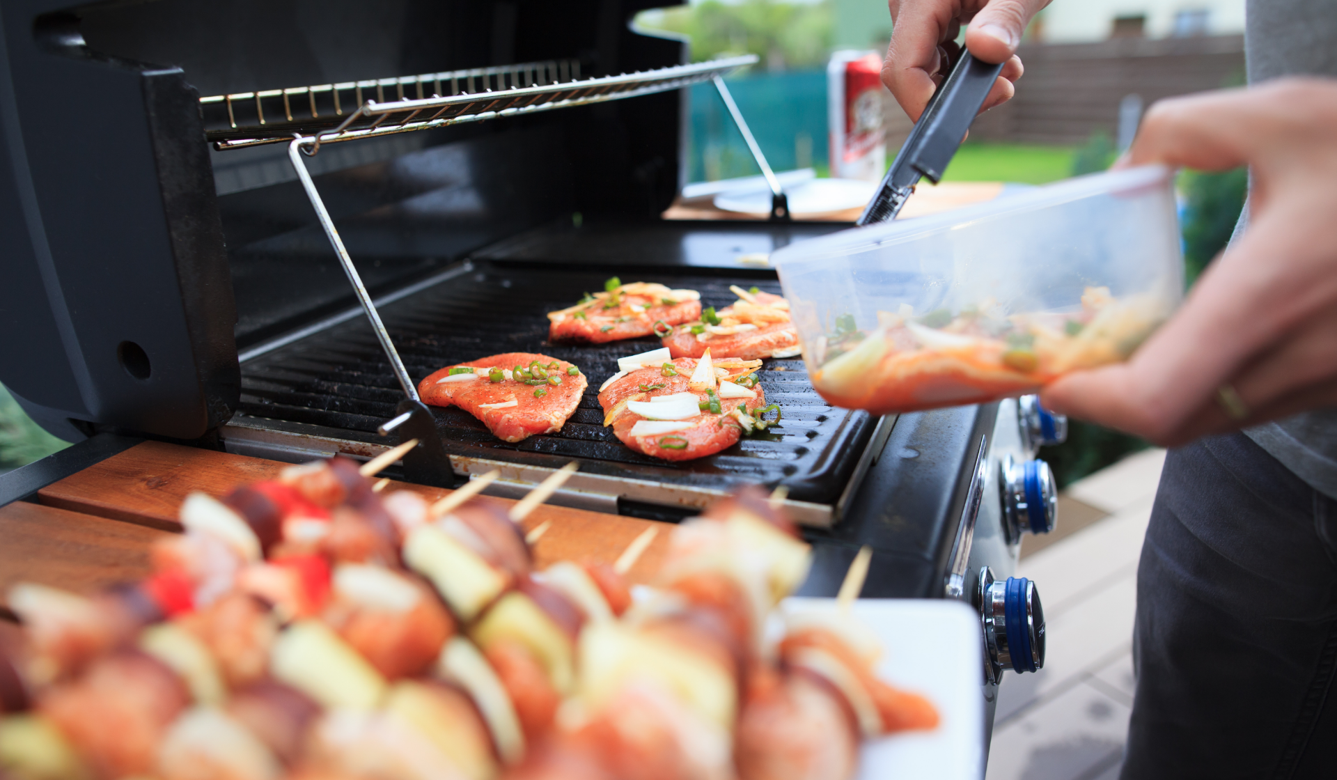 Eine Person legt mariniertes Fleisch aus einer Plastik Box auf einen Gasgrill.