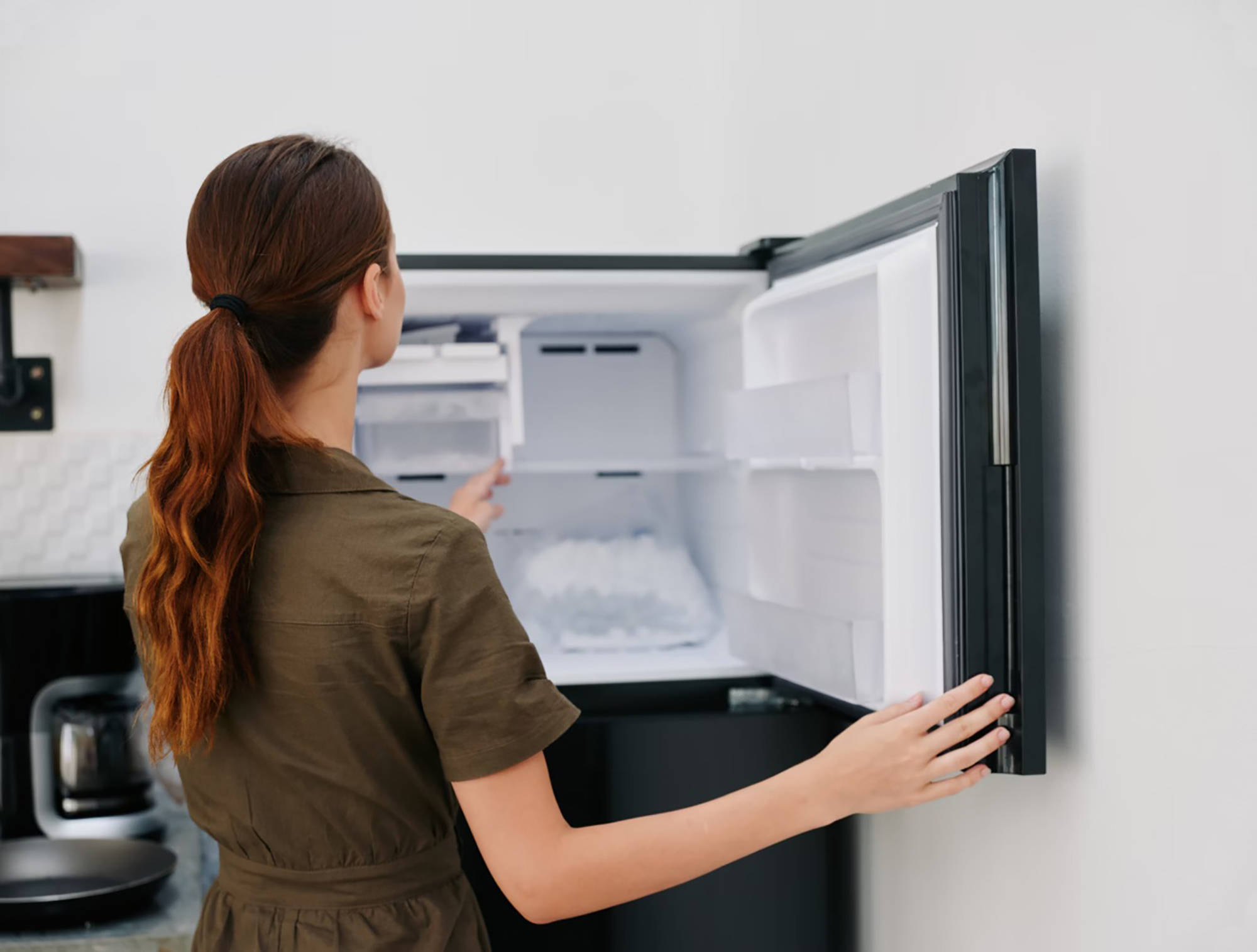 Frau öffnet einen mit Eiswürfeln gefüllten Gefrierschrank in einer modernen Küche.