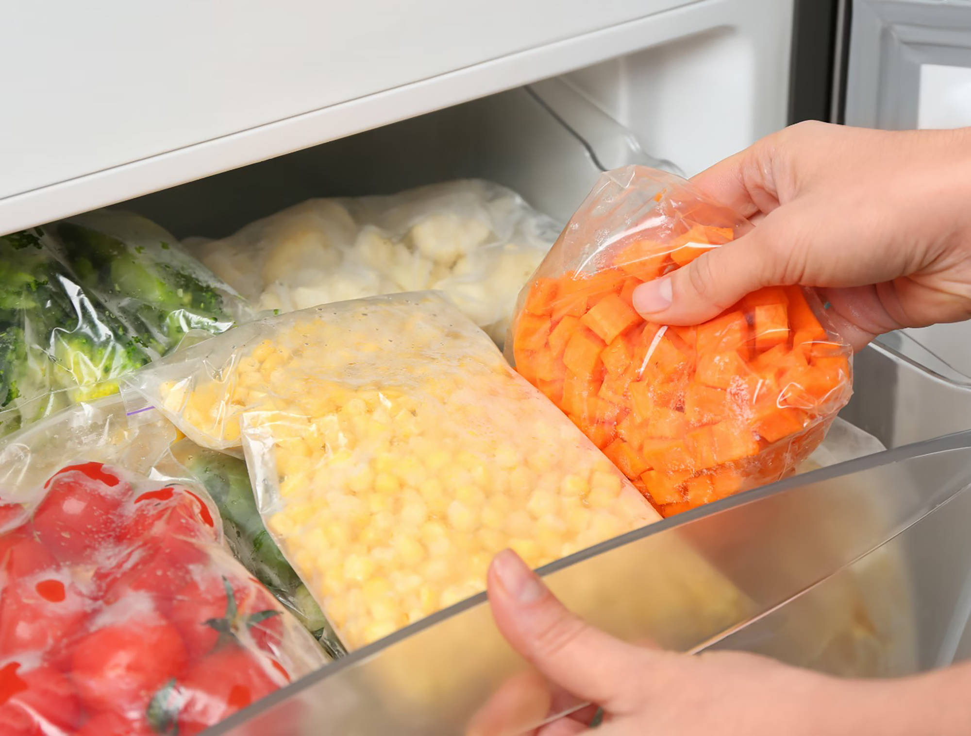Person legt gefrorene und in einer Plastiktüte verpackte Möhrenwürfel in ein Gefrierfach.