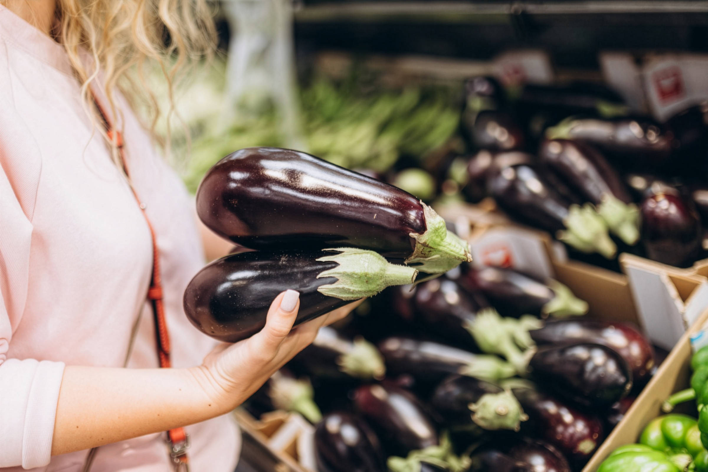 Frau in rosa Pullover hält zwei Auberginen beim Einkaufen im Supermarkt.
