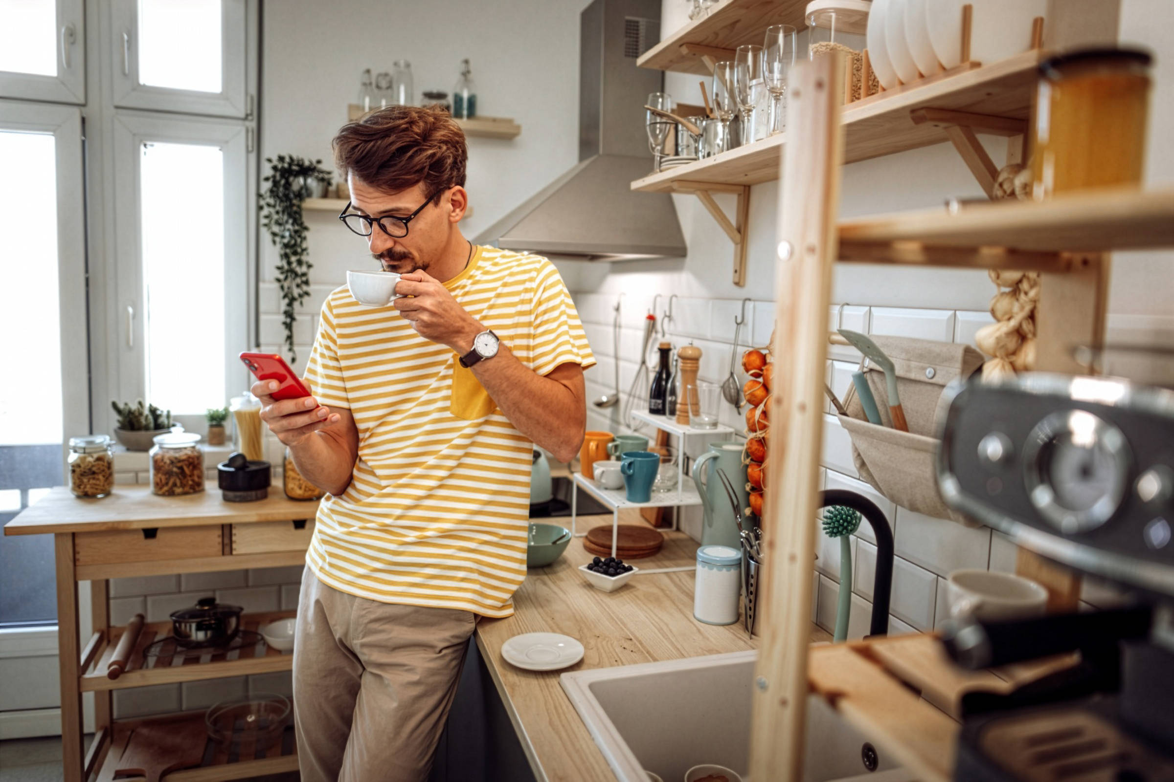 Mann in gestreiftem Shirt trinkt eine Tasse Kaffee und schaut in seinem Smartphone nach Sonderangeboten.