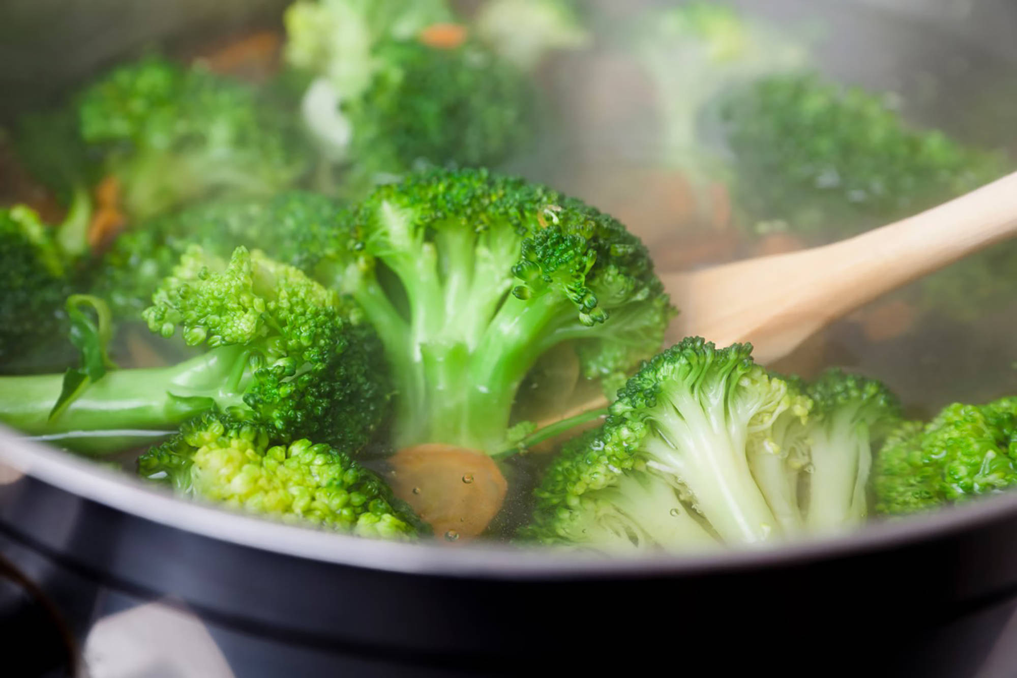 Frischer Brokkoli wird in einer Pfanne mit einem Holzlöffel gedünstet, um ihn schonend zuzubereiten. 