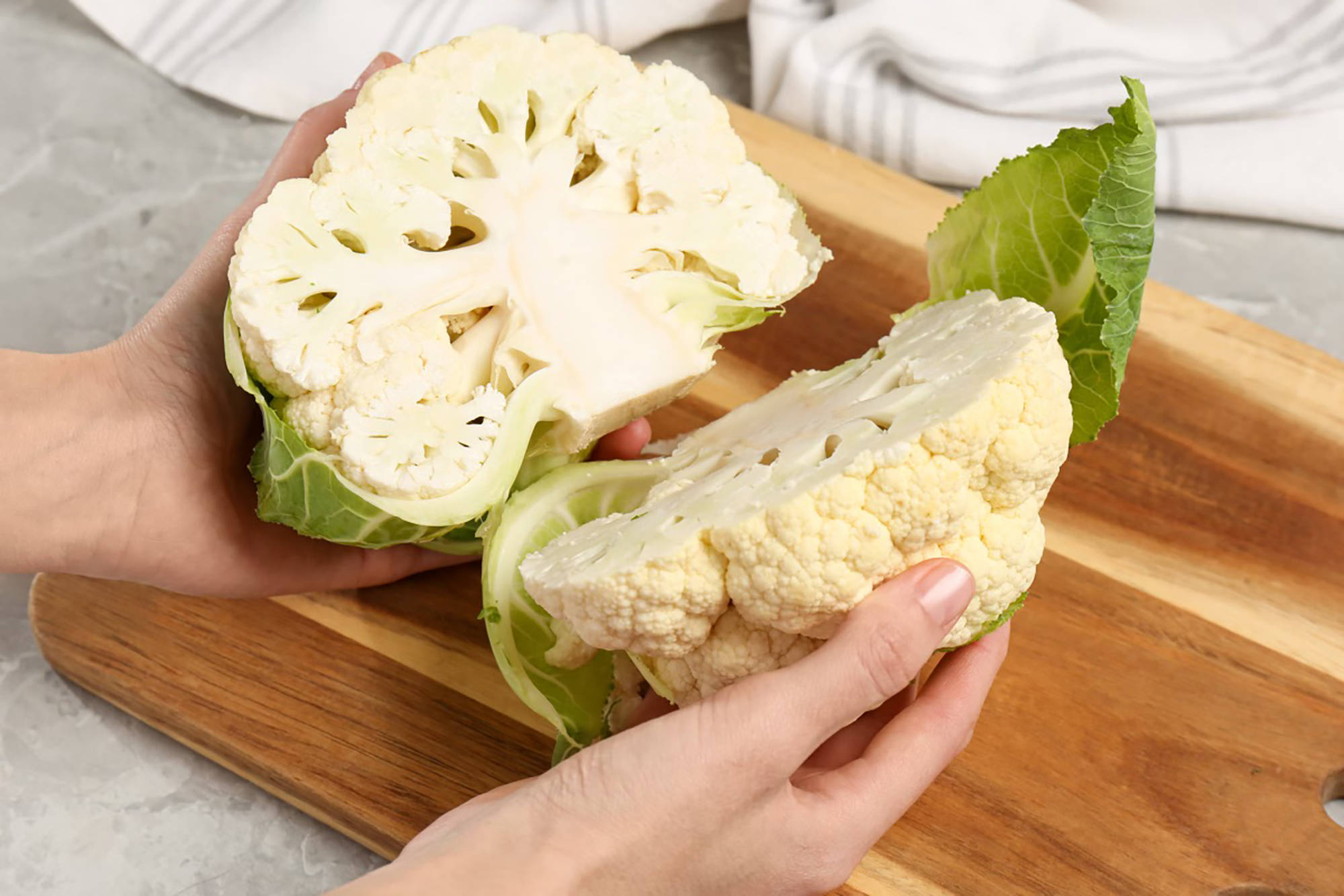 Zwei Hälften eines frischen Blumenkohls werden auf einem Schneidebrett für die Zubereitung vorbereitet.