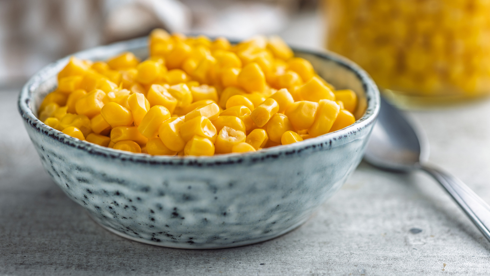Maiskörner in Schüssel, Glas und Löffel.