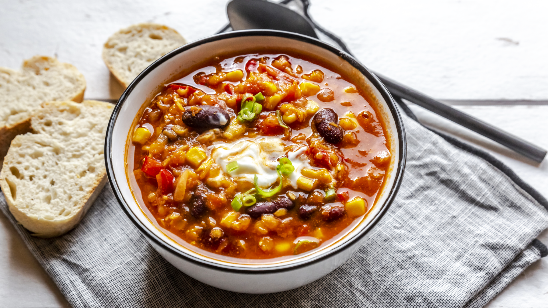 Schüssel mit herzhafter Gemüsesuppe, Brot und Löffel.