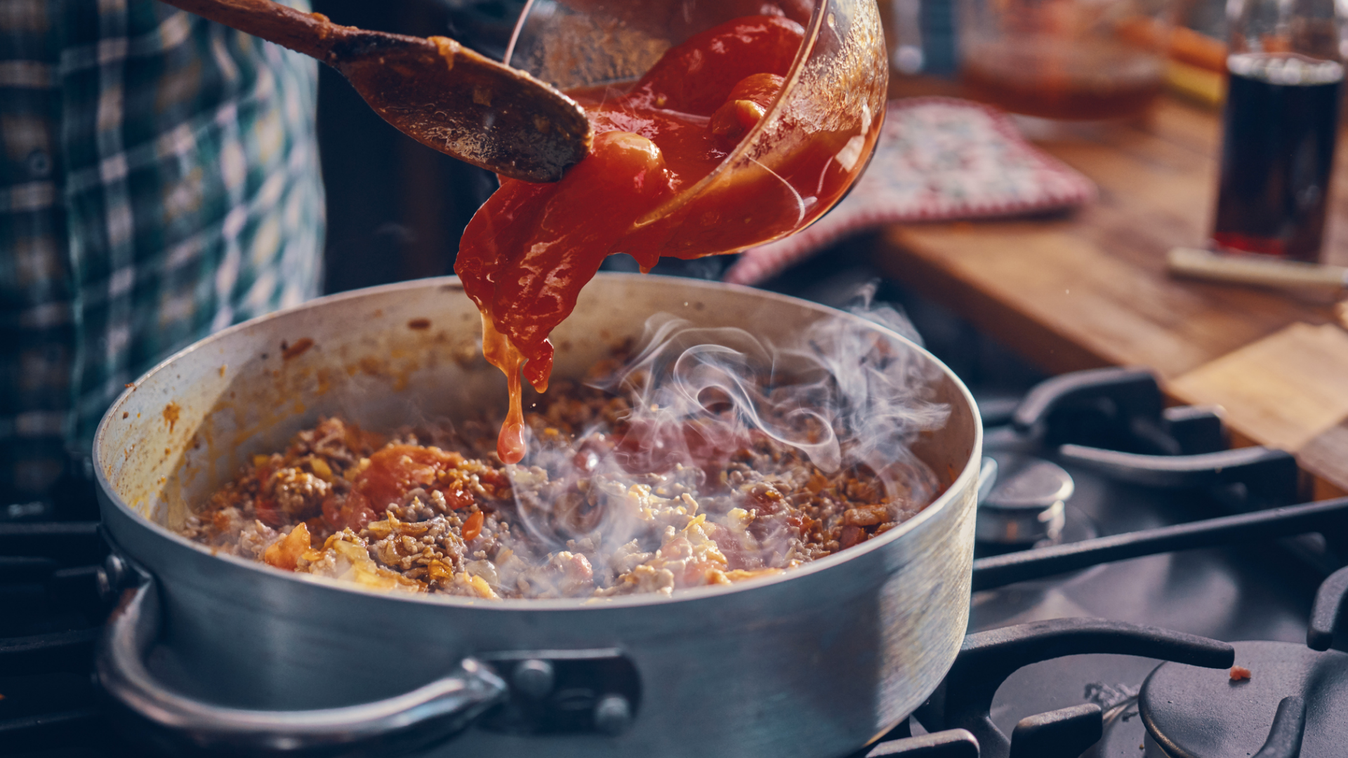 Tomatensoße wird in einen Topf mit Hackfleisch gegossen.