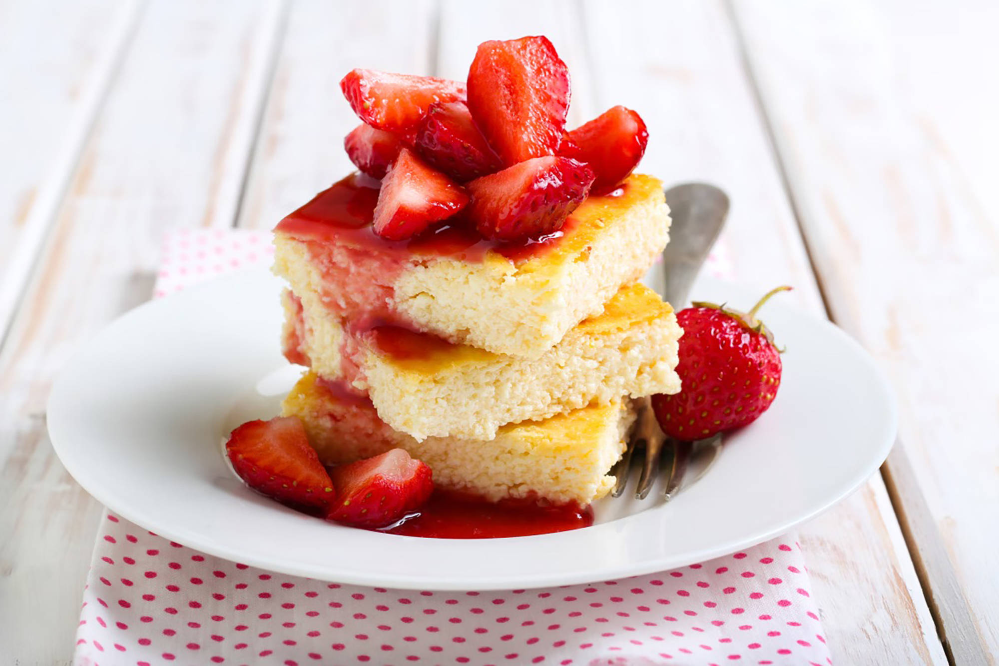 Saftige glutenfreie Kuchenstücke auf einem Teller gestapelt mit frischen Erdbeeren und Sauce getoppt.