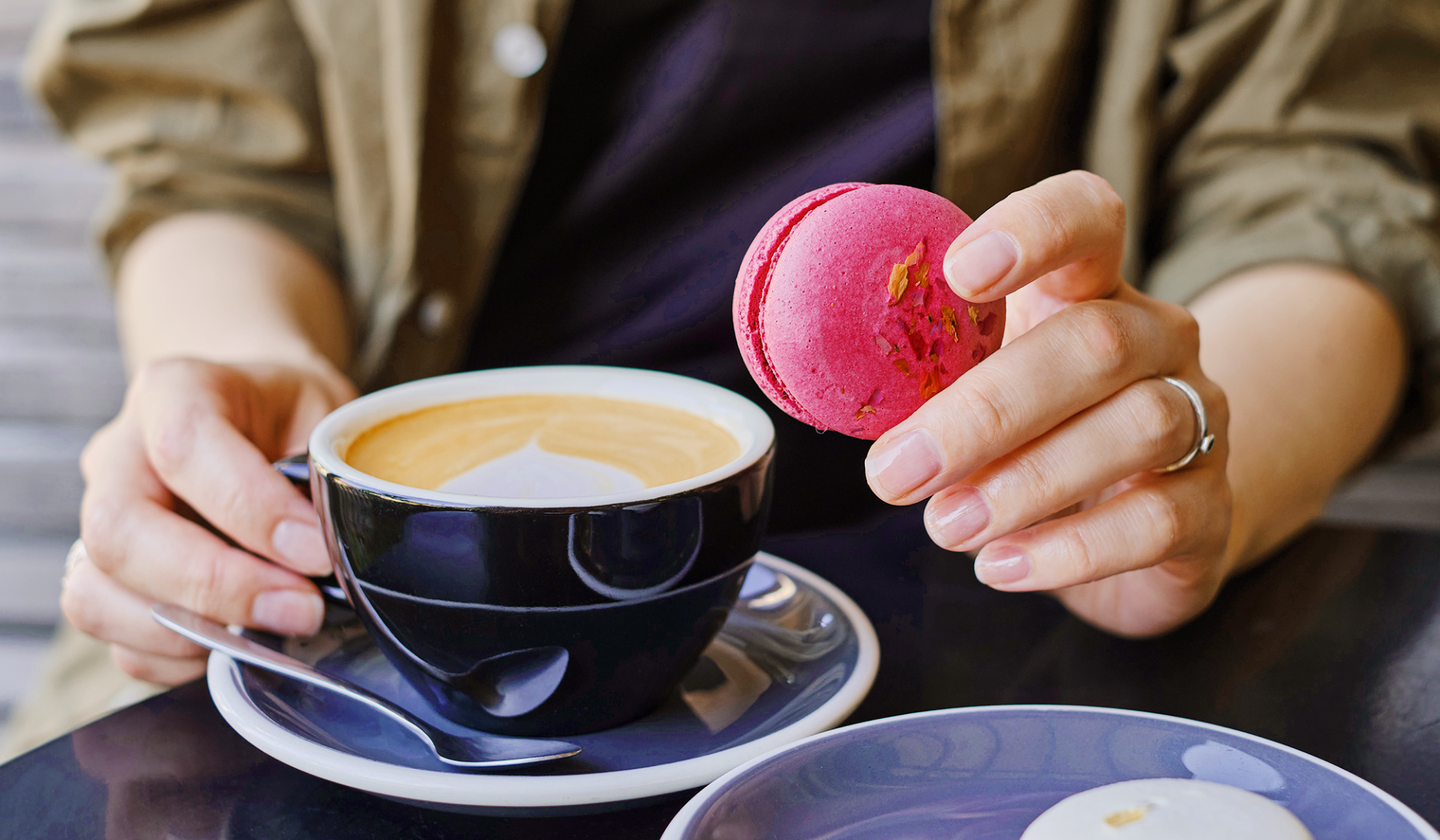 Person hält rosa Macaron und Kaffeetasse mit Latte Art.