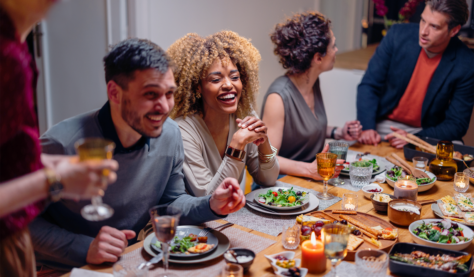 Lachende Freunde genießen Abendessen an festlich gedecktem Tisch.