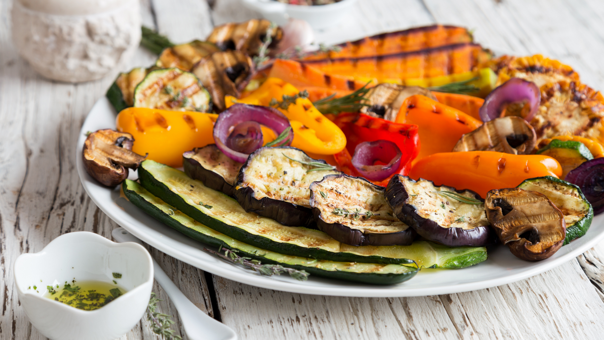 Teller mit gegrilltem Gemüse auf weißem Holztisch.