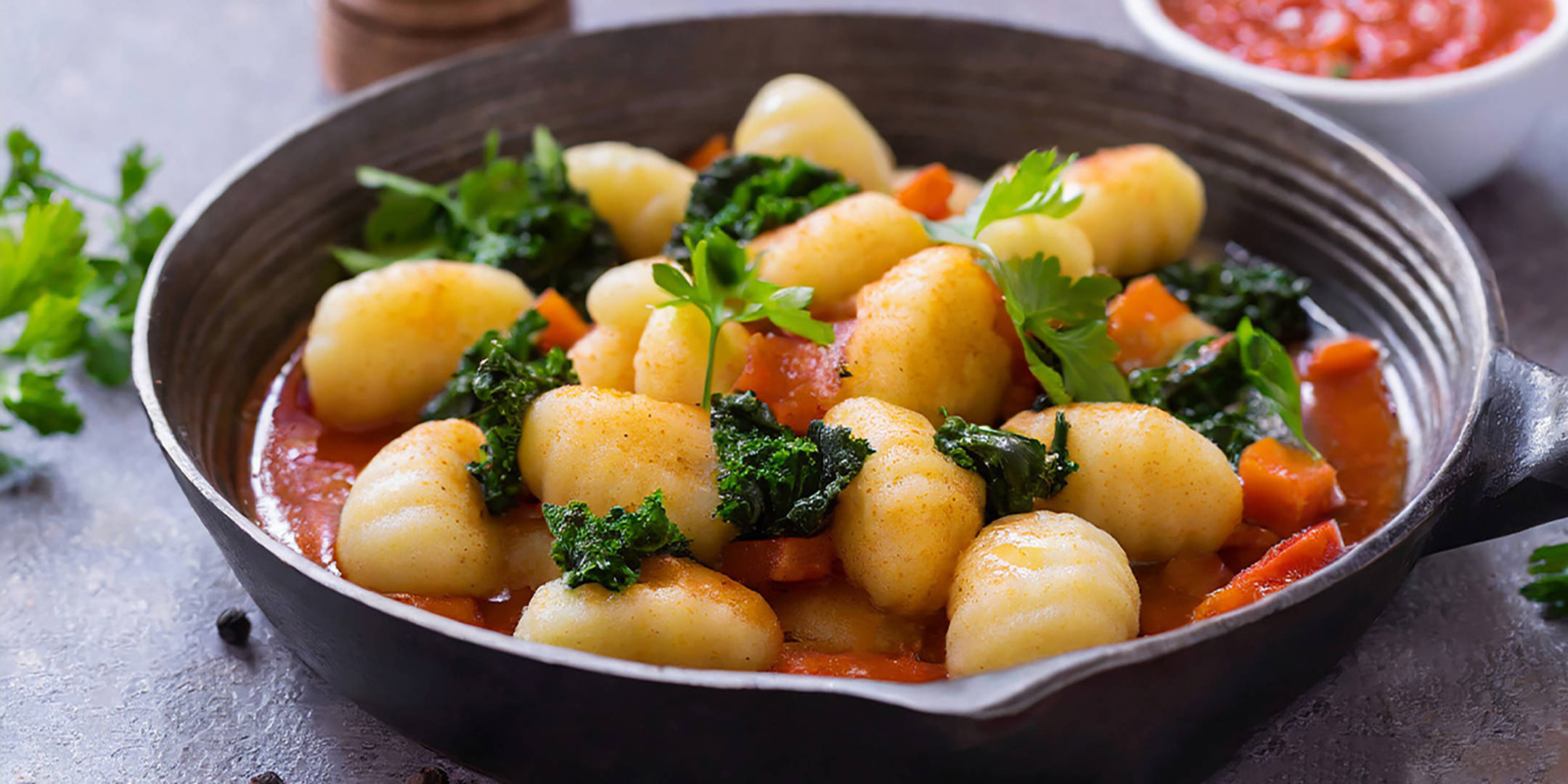 Gnocchi mit Grünkohl, Karotten und Tomatensauce in einer Pfanne.
