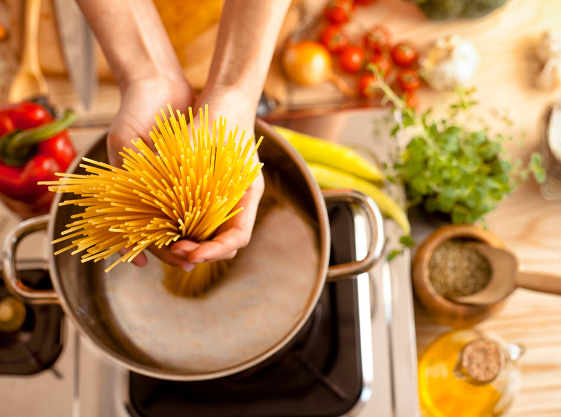Person gibt eine Hand voll roher Spaghetti-Nudeln in einen Topf mit heißem Wasser.