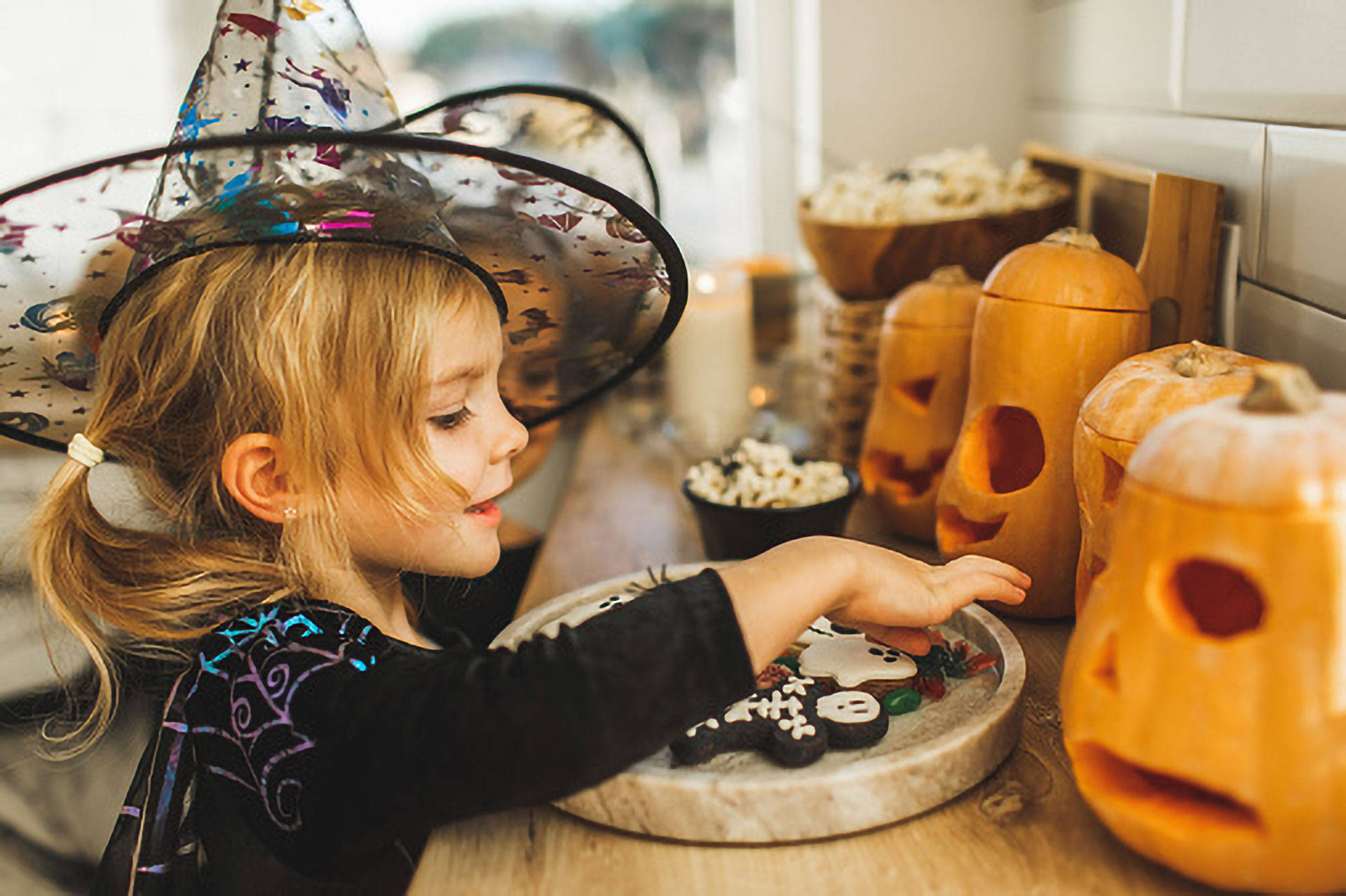Ein Kind in einem Halloween Kostüm vor einem mit geschnitzten Kürbissen dekorierten Tisch. 