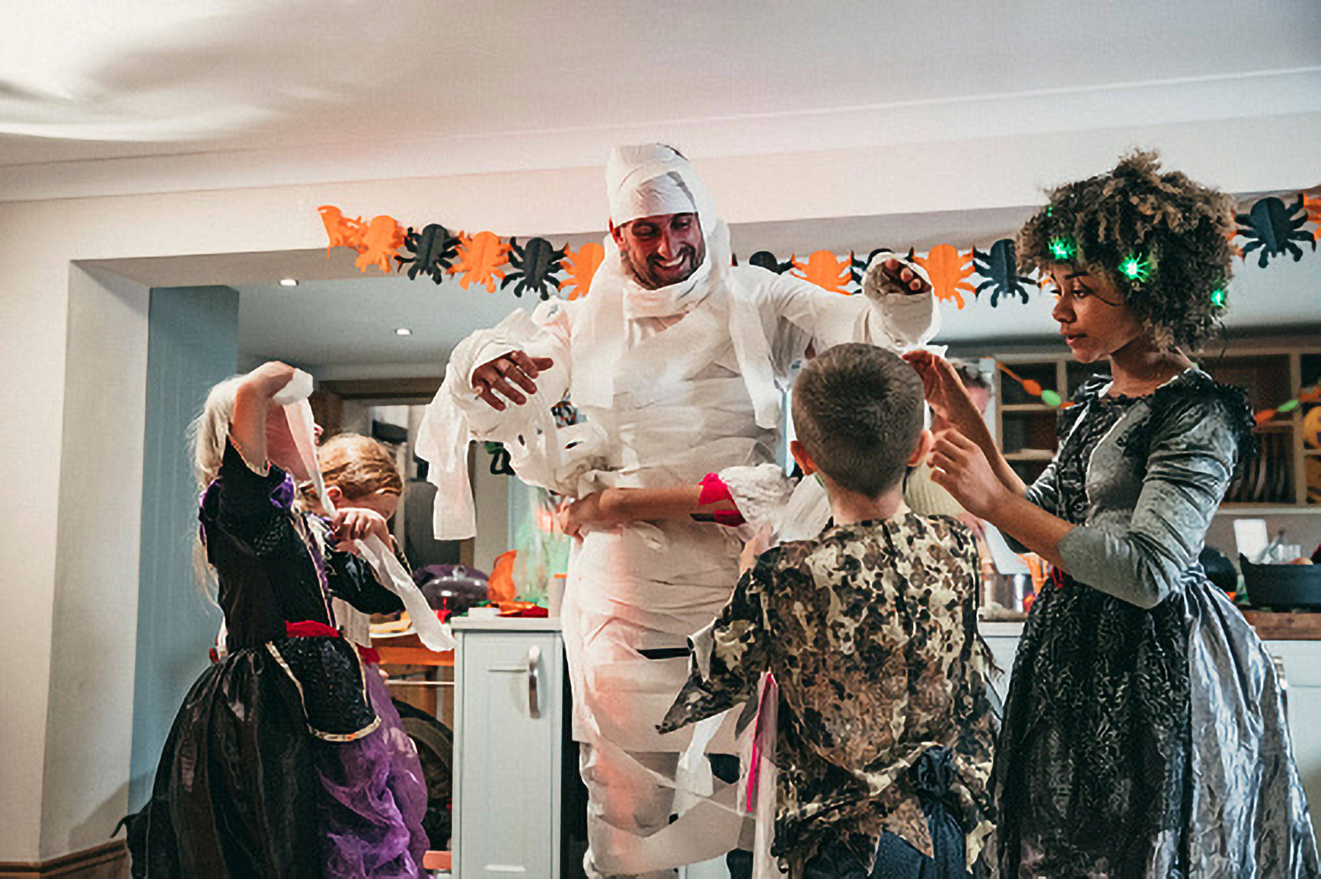 Kinder wickeln einen Mann für ein Halloween Kostüm mit Toilettenpapier ein. 