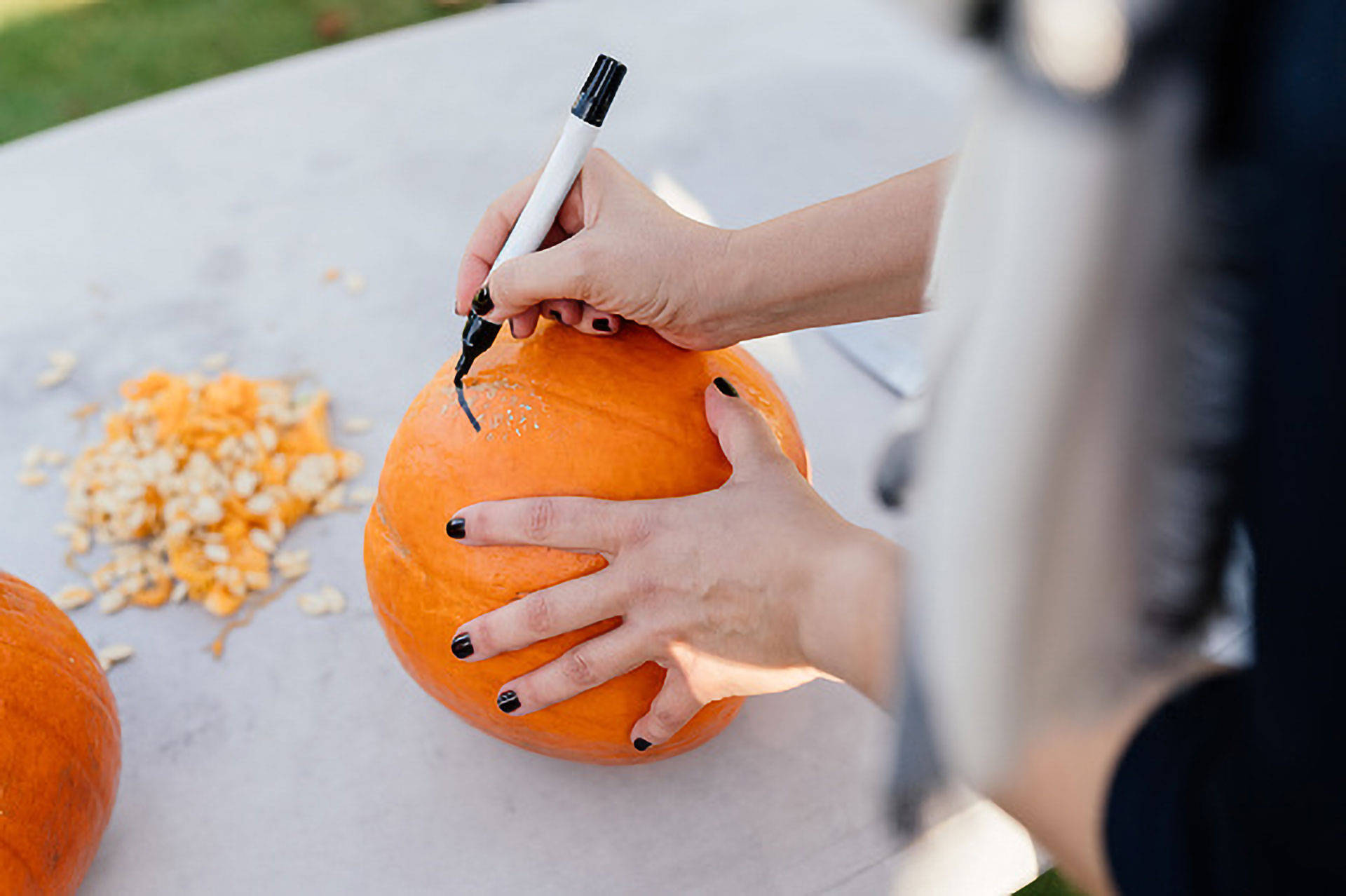 Eine Frau malt auf einen Kürbis, damit dieser geschnitzt werden kann.