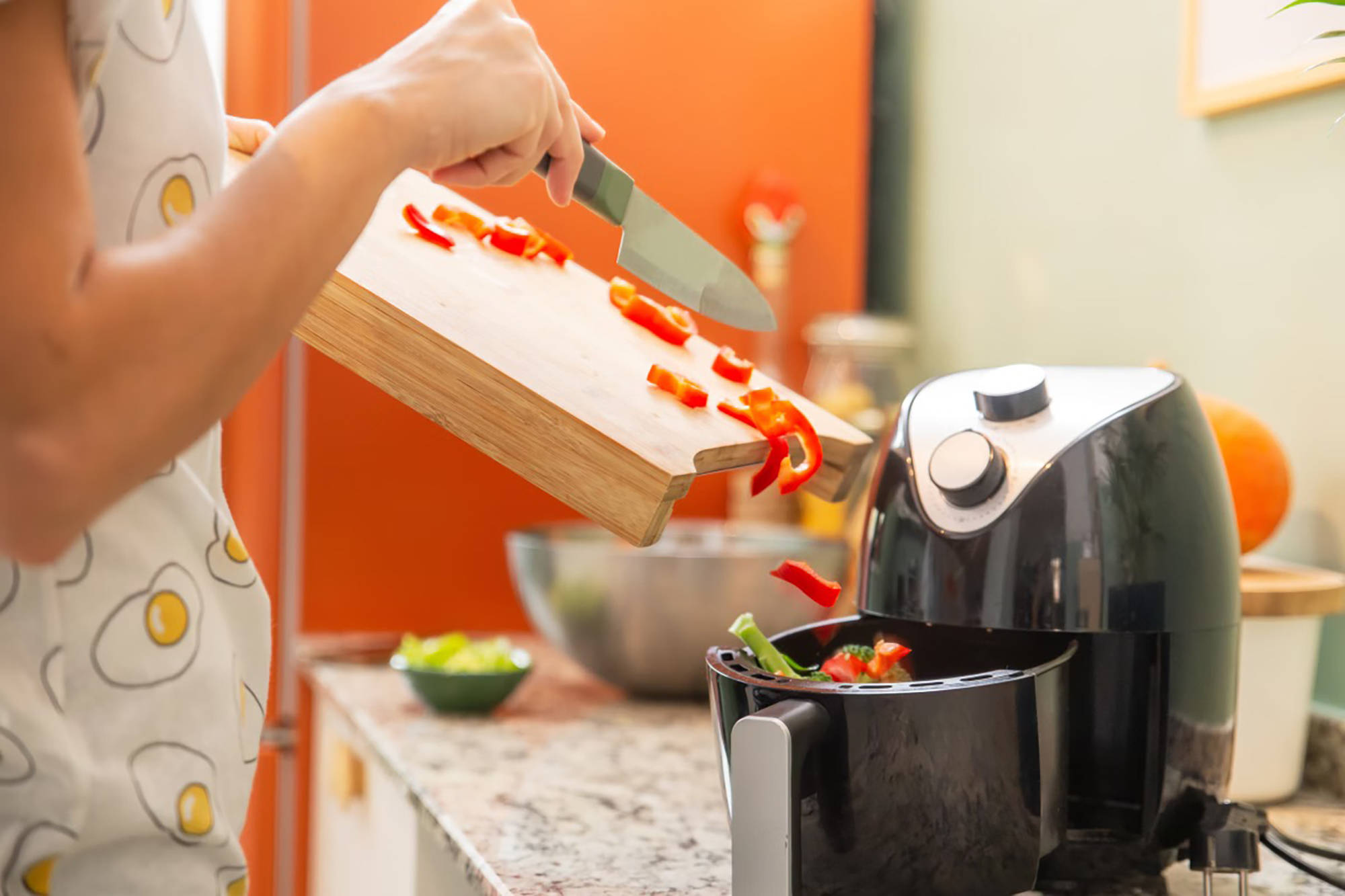 Eine Frau gibt geschnittene Paprika von einem Holzbrett in eine Heißluftfritteuse.