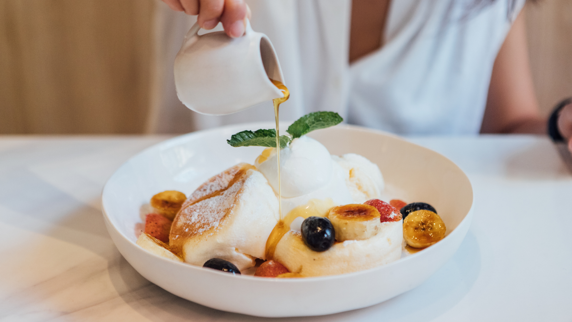 Honig wird auf Soufflé-Pancakes mit Früchten und Eiscreme gegossen.