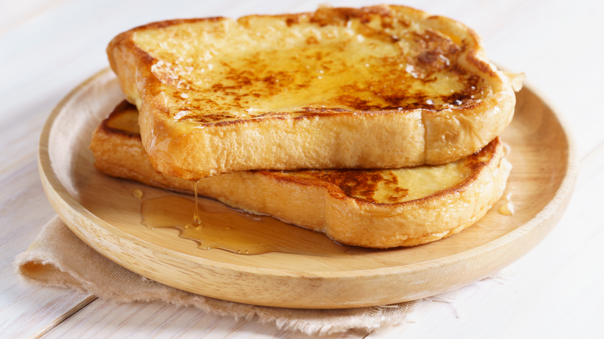 Zwei French Toasts mit tropfendem Honig auf Holzteller.