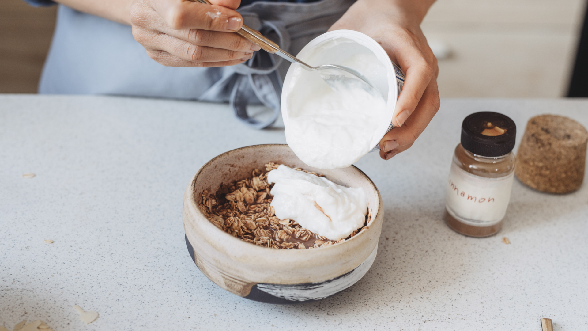 Person bereitet Müsli mit Joghurt und Zimt zu.