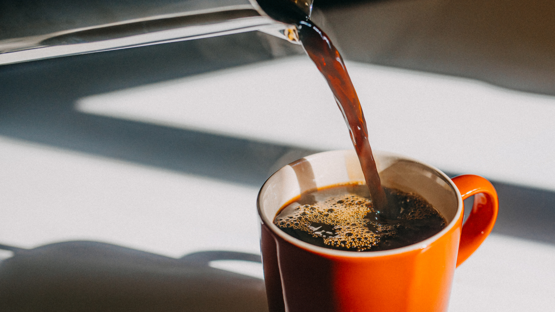 Kaffee wird in eine orangefarbene Tasse gegossen.