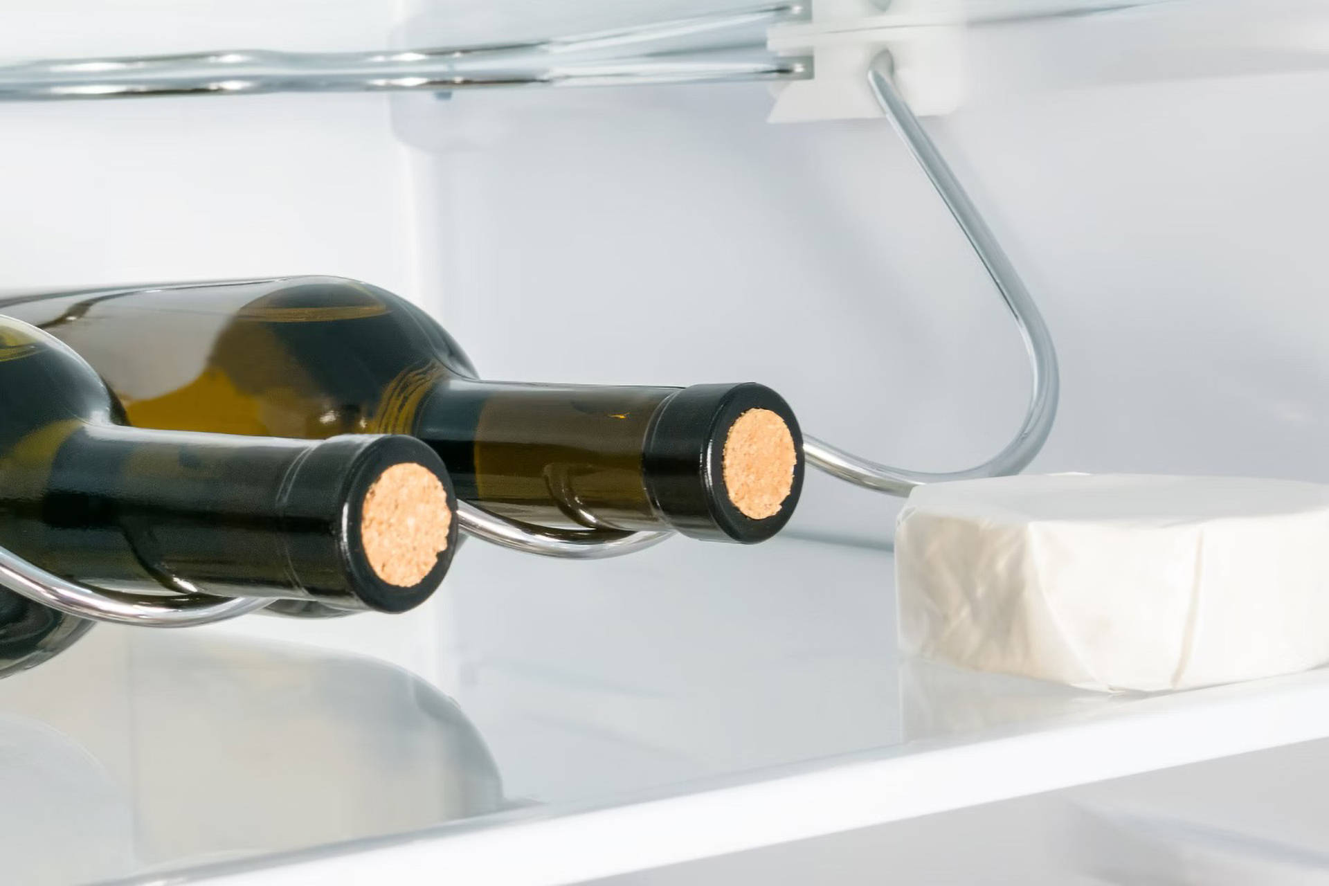 Zwei Weinflaschen und ein Stück Käse im Kühlschrank.