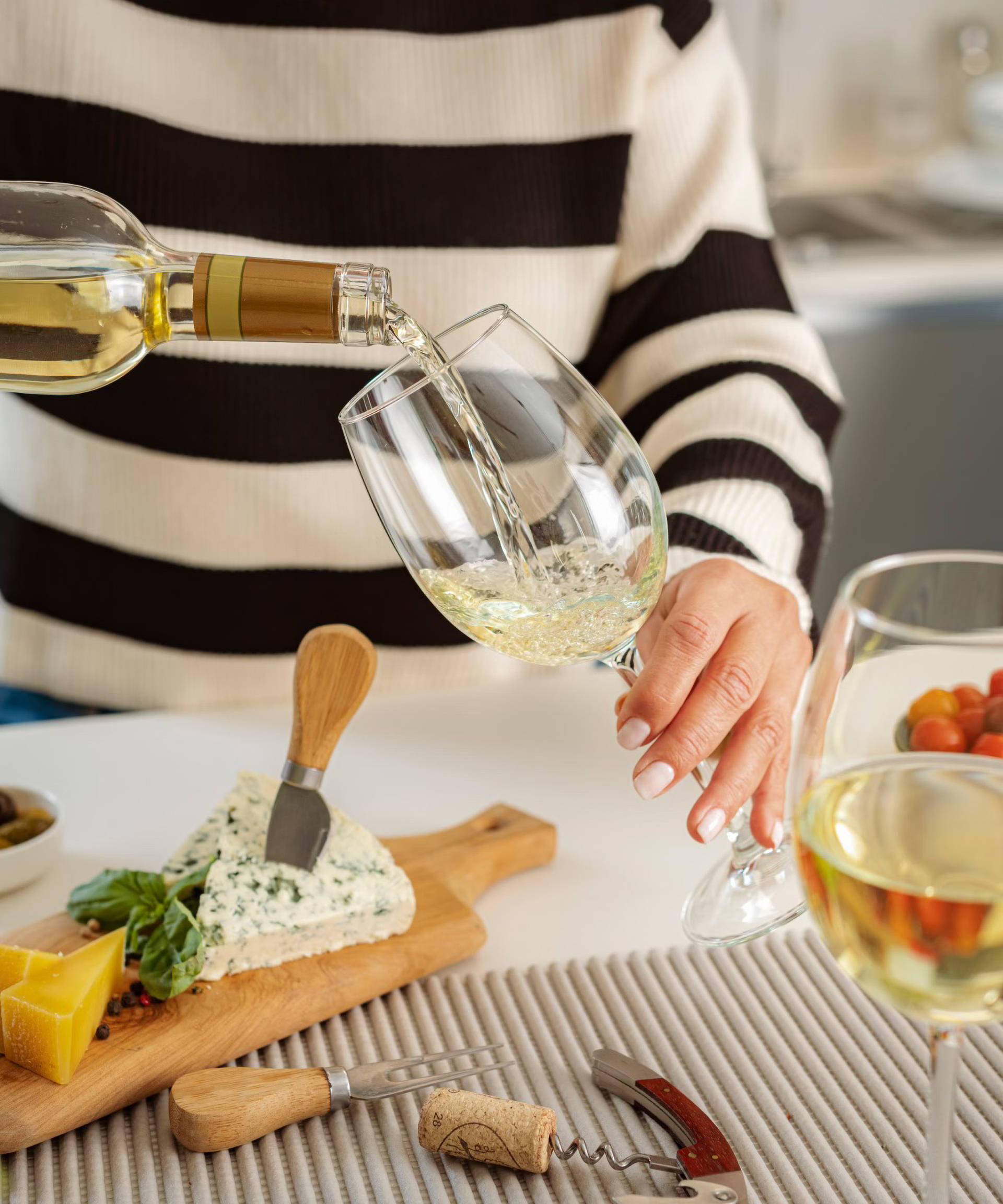 Eine Frau schenkt zu einer Käseplatte Weißwein in Gläser ein.