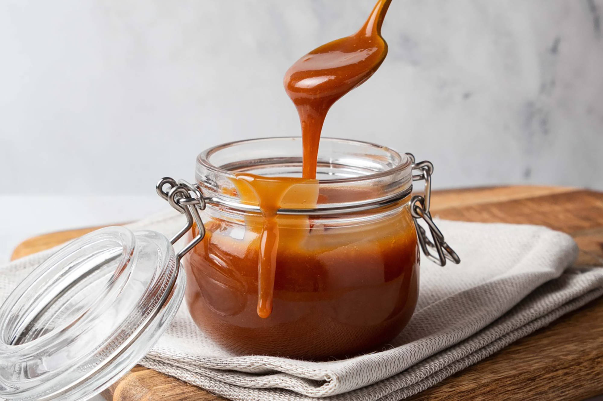 Flüssiges Karamell tropft von einem Löffel in ein Glas mit Schraubverschluss.