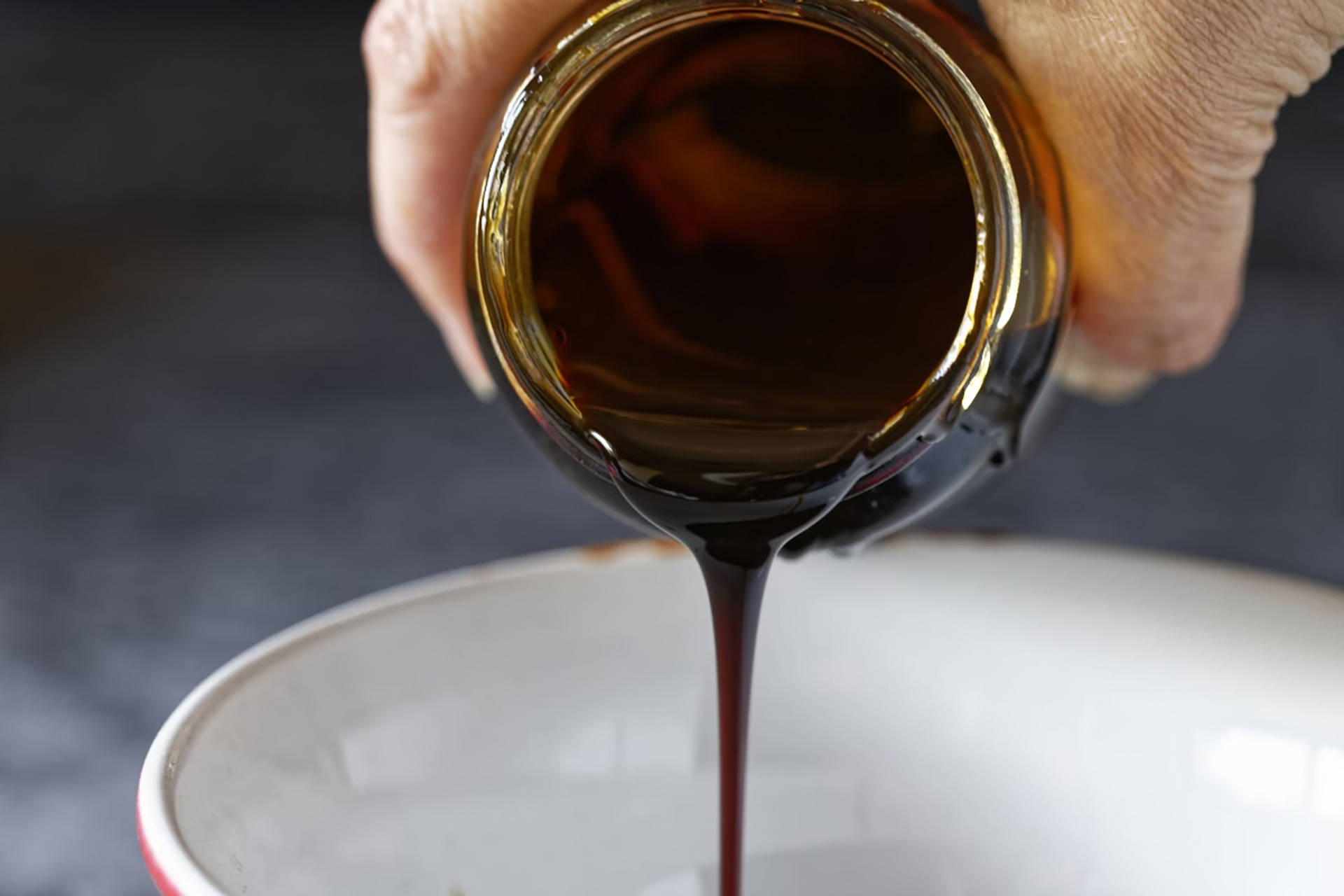 Hand gießt dunklen Sirup aus Glas in Schüssel.