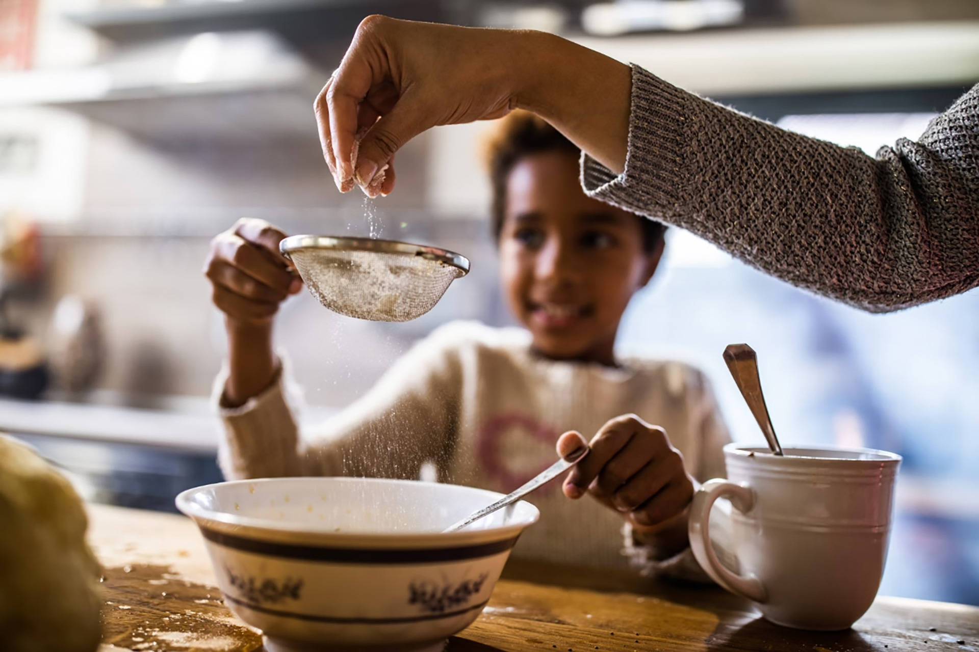 Erwachsene Hand siebt Puderzucker in Kinderschüssel beim Backen.
