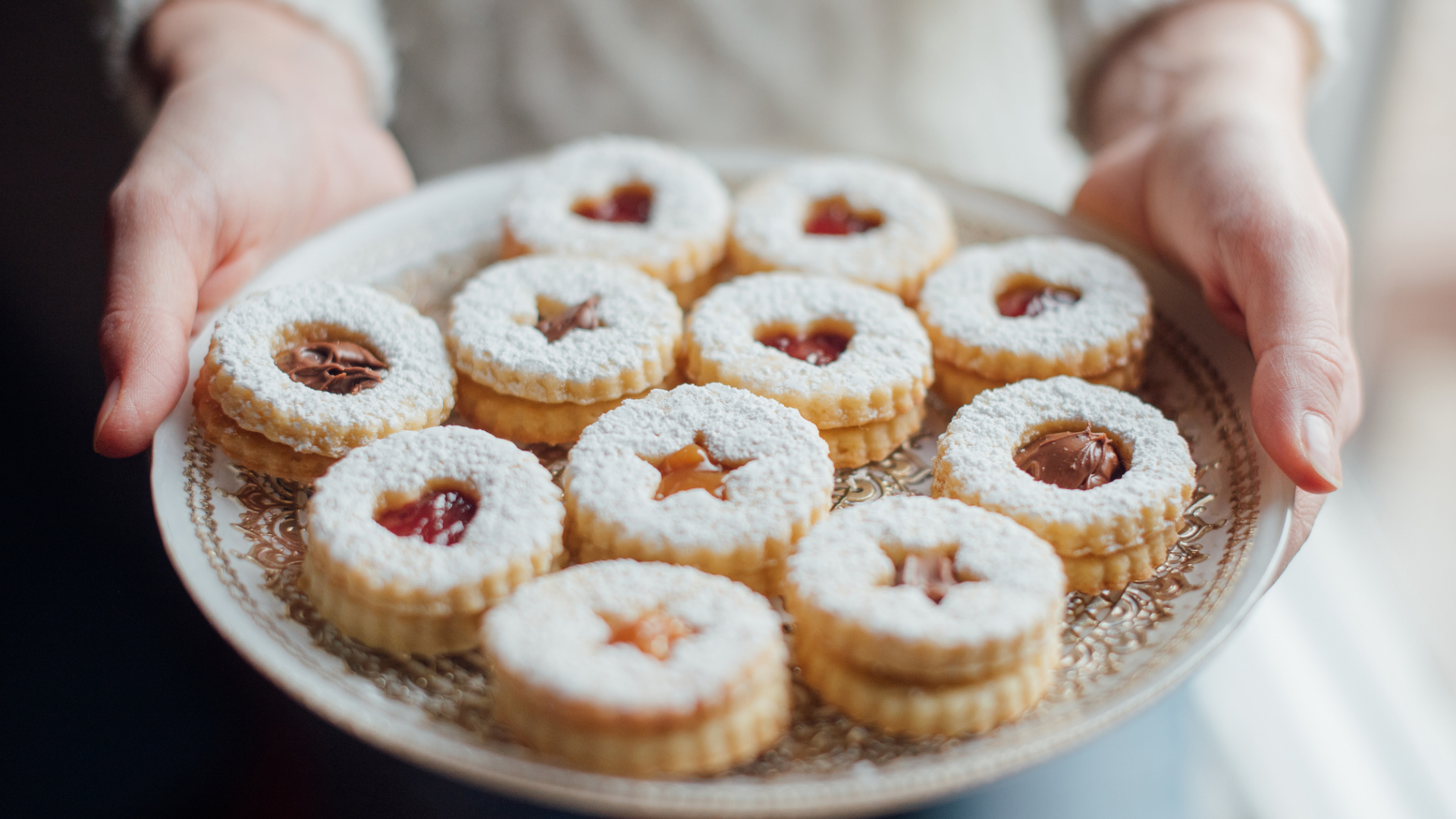 Hände halten Teller mit Linzer Keksen, Puderzucker.
