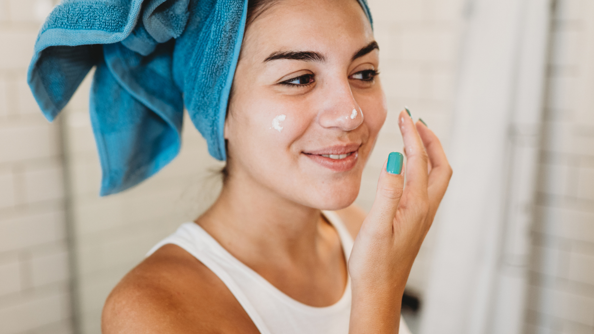 Frau mit blauem Handtuch trägt Gesichtscreme auf.