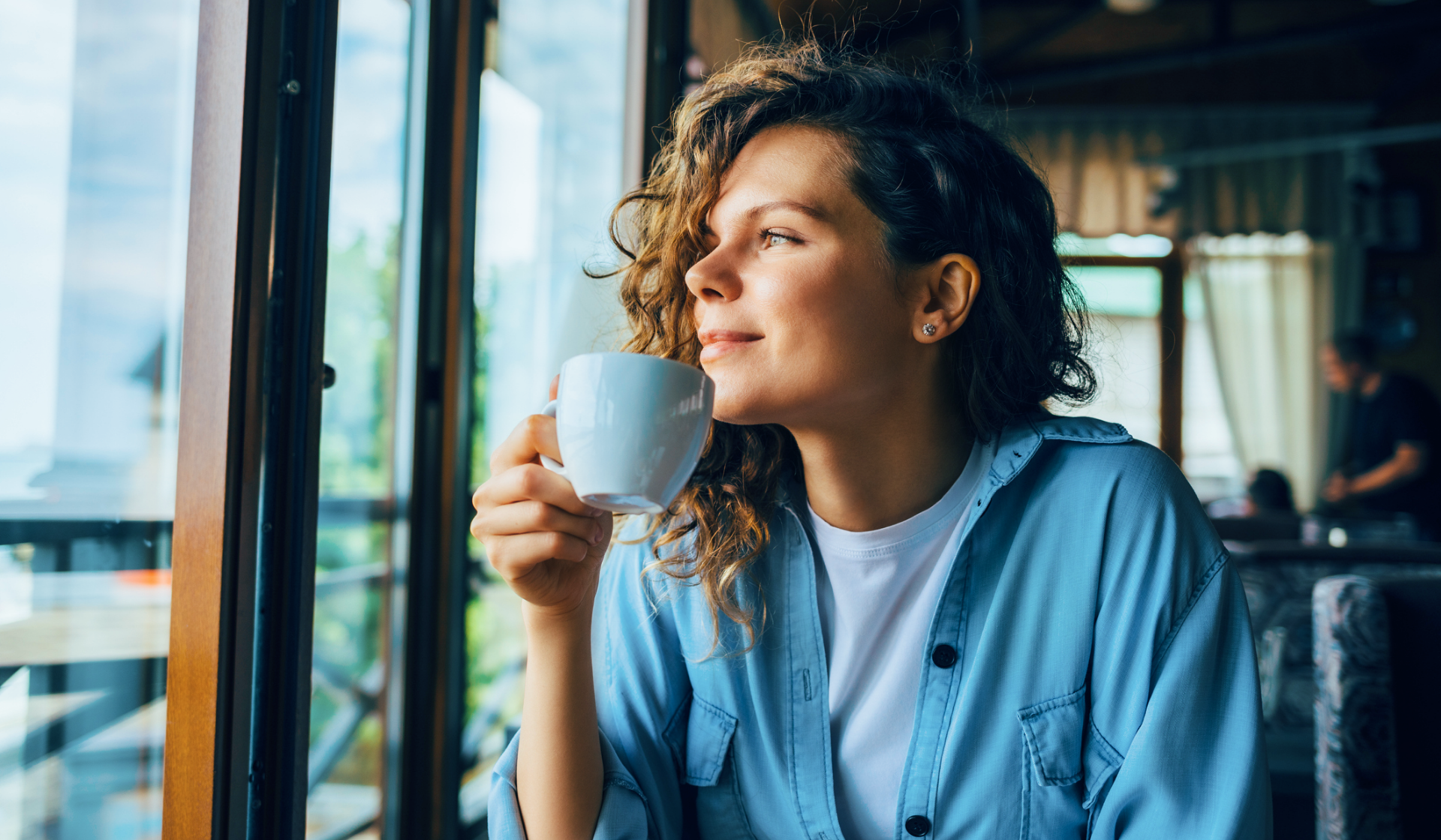 Frau mit Teetasse in der Hand schaut zufrieden aus dem Fenster