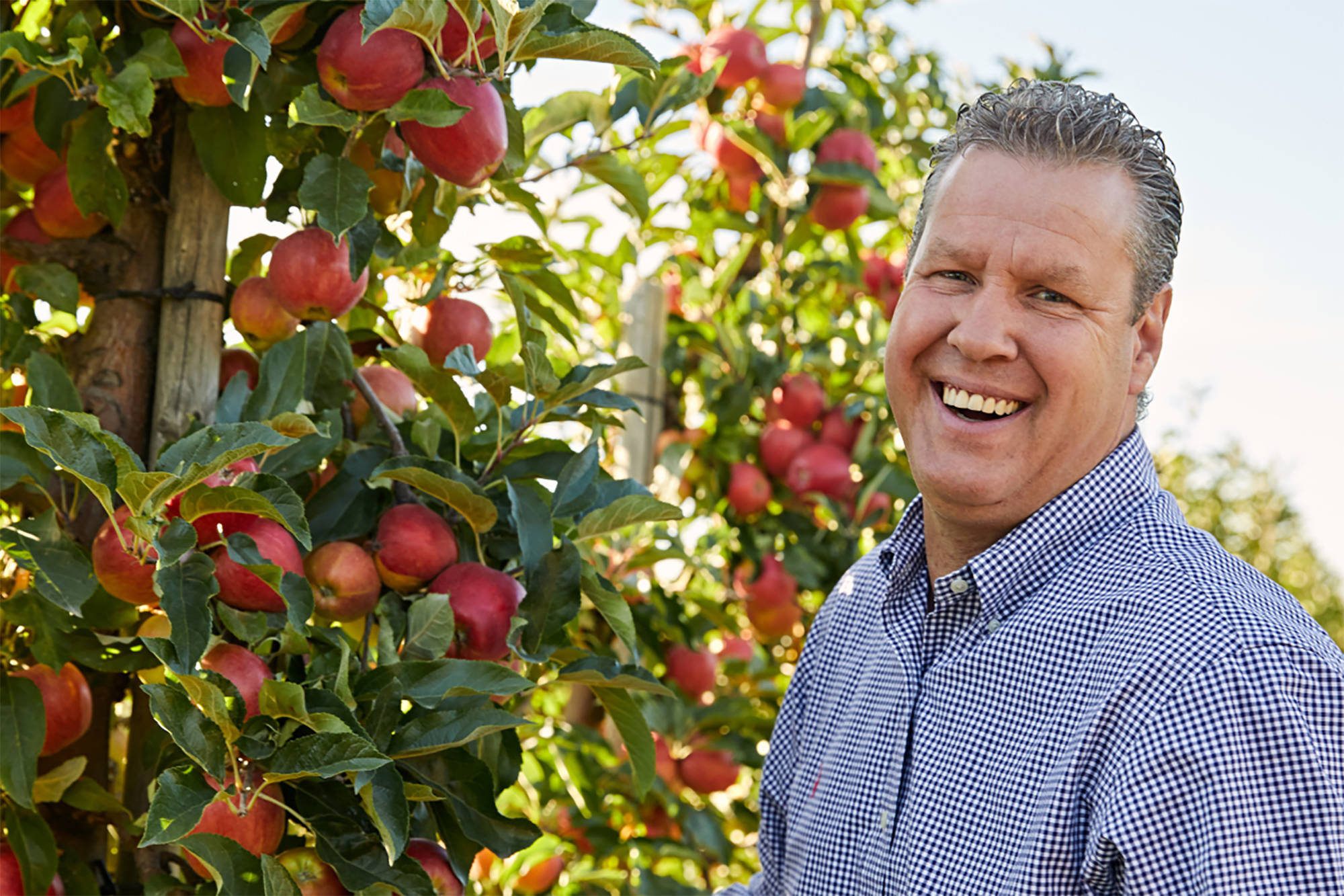 Apfelbauer lächelnd vor seinen Äpfelbäumen.