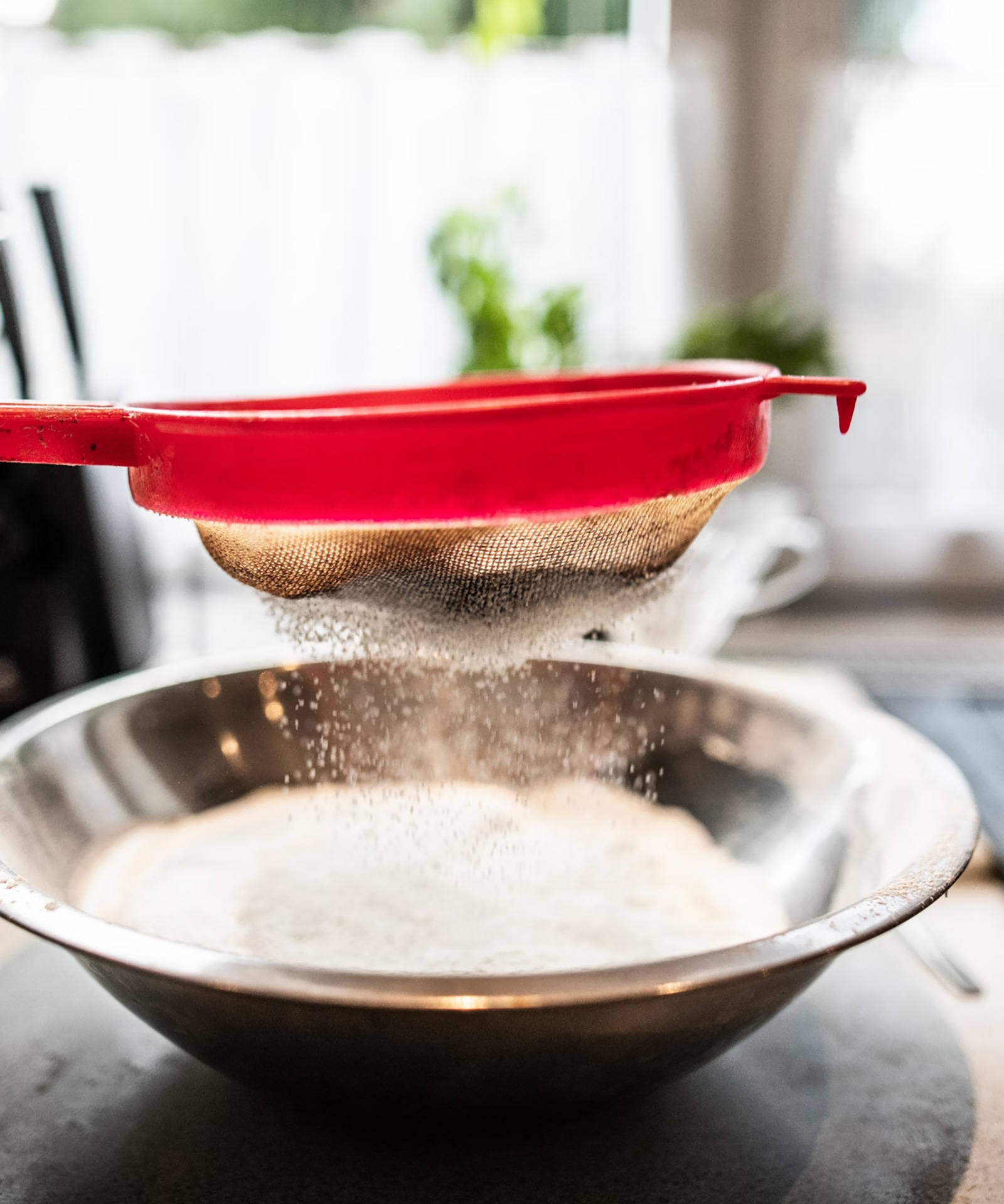 Rotes Sieb siebt Mehl in eine Schüssel.