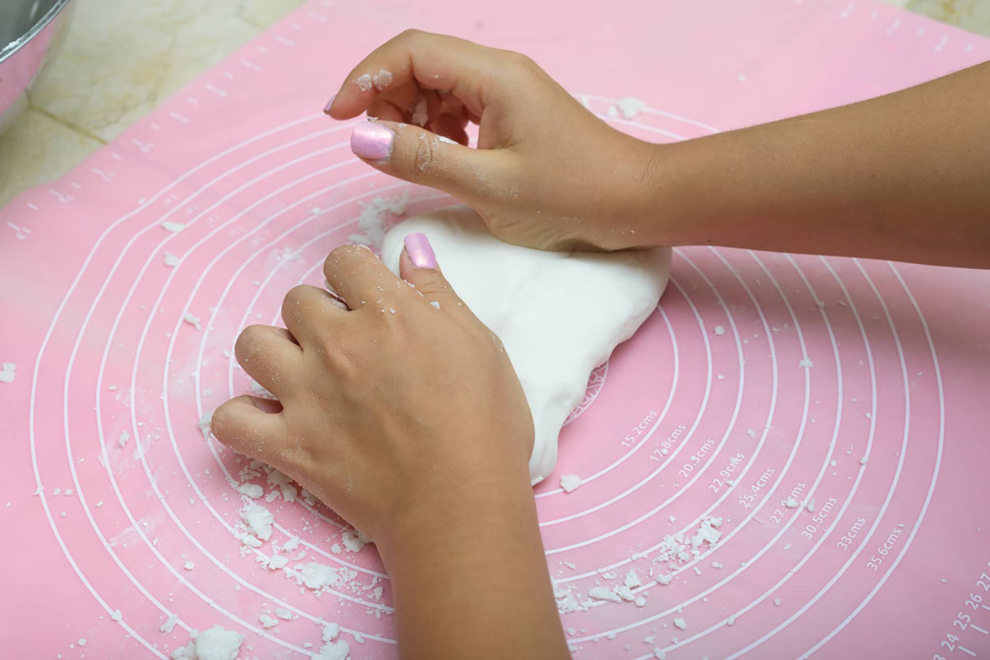 Jemand knetet mit den Händen einen weißen Teig auf einer rosa Backunterlage mit kreisförmigen Markierungen und Mehlreste
