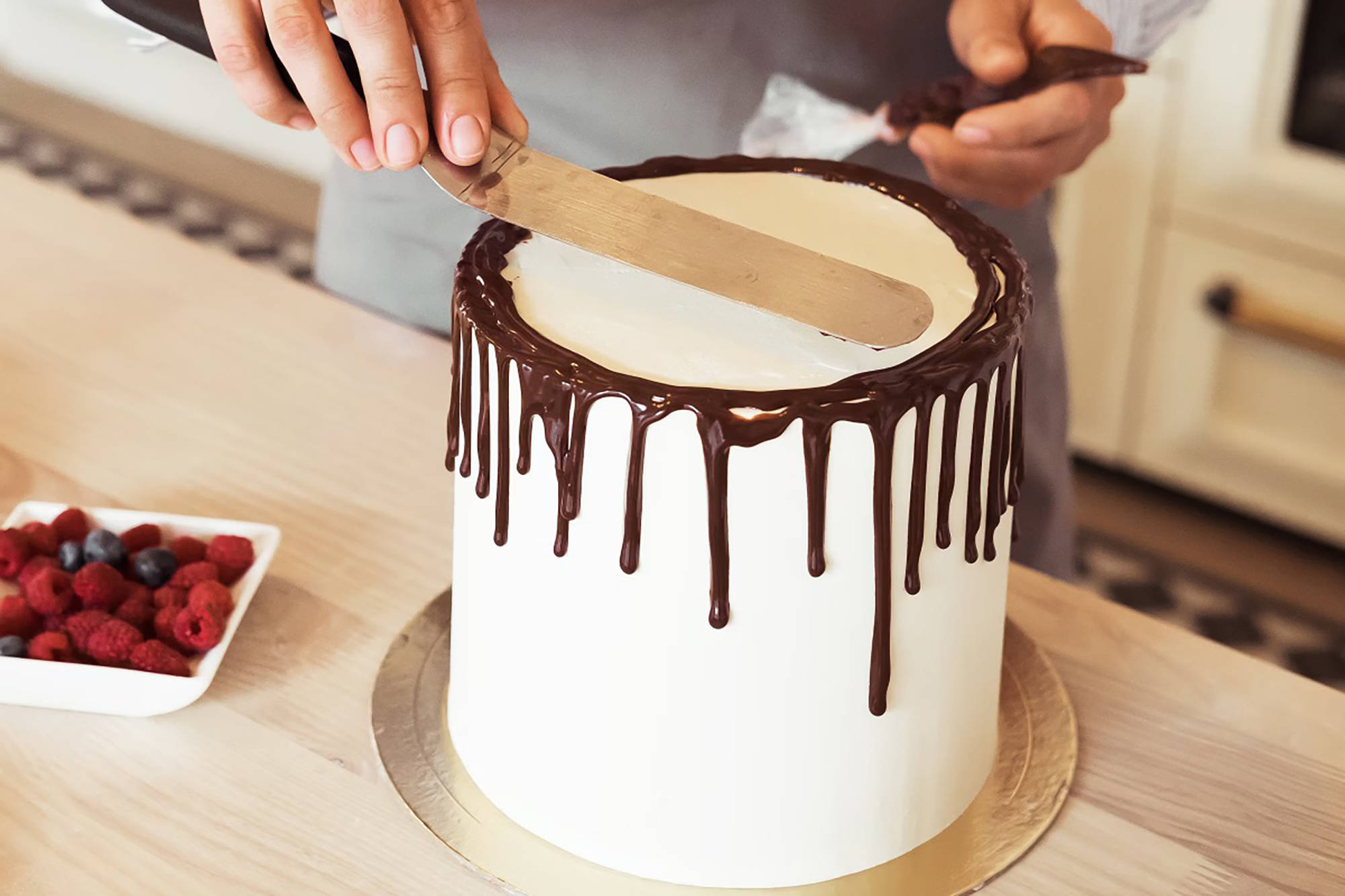 Konditor glättet weiße Torte mit am Tortenrand herabtropfender Schokoladenglasur.