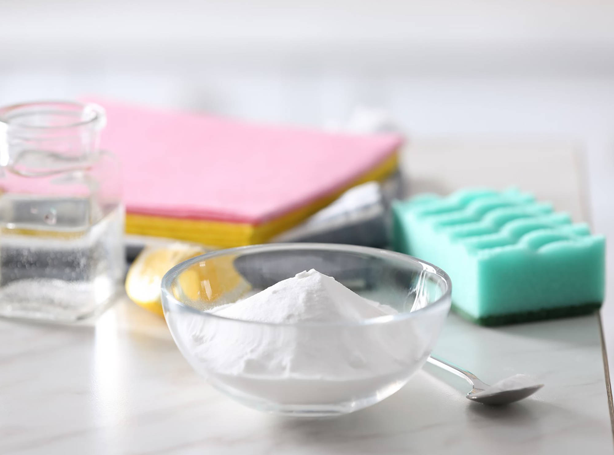 Natron in Glasschüssel, Essigflasche, Zitronenscheibe, Schwämme und Reinigungstücher.